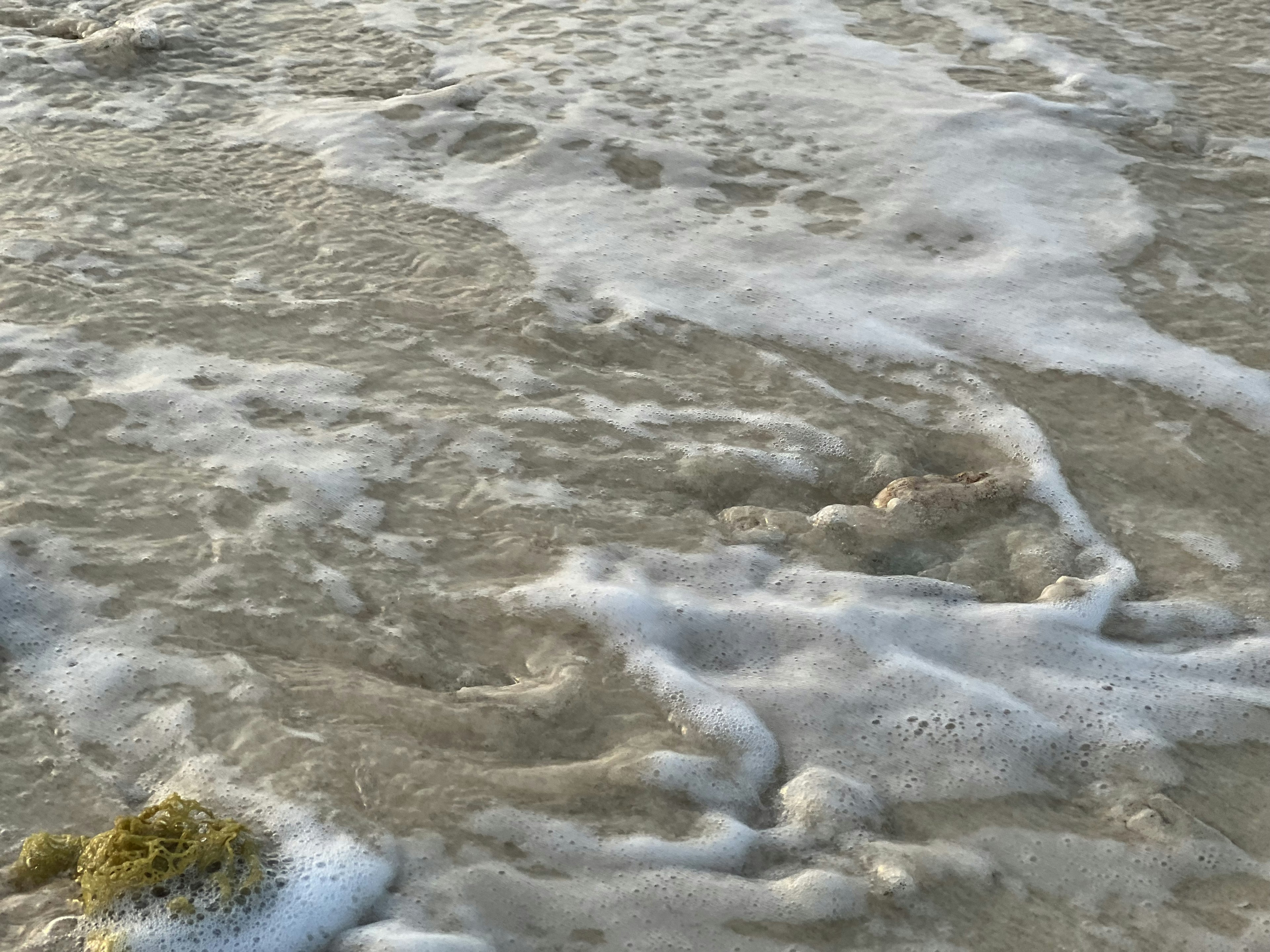 Superficie dell'acqua con onde e schiuma vicino a una spiaggia di sabbia