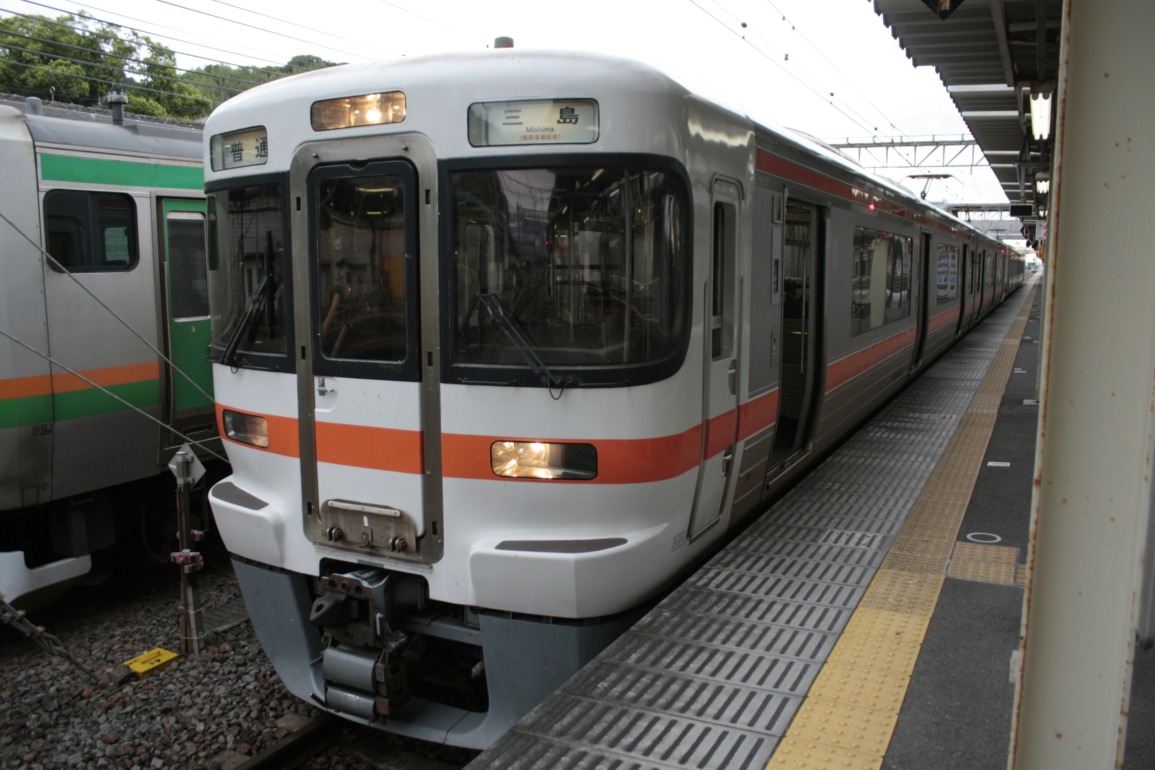 Treno moderno con strisce bianche e arancioni fermo alla stazione