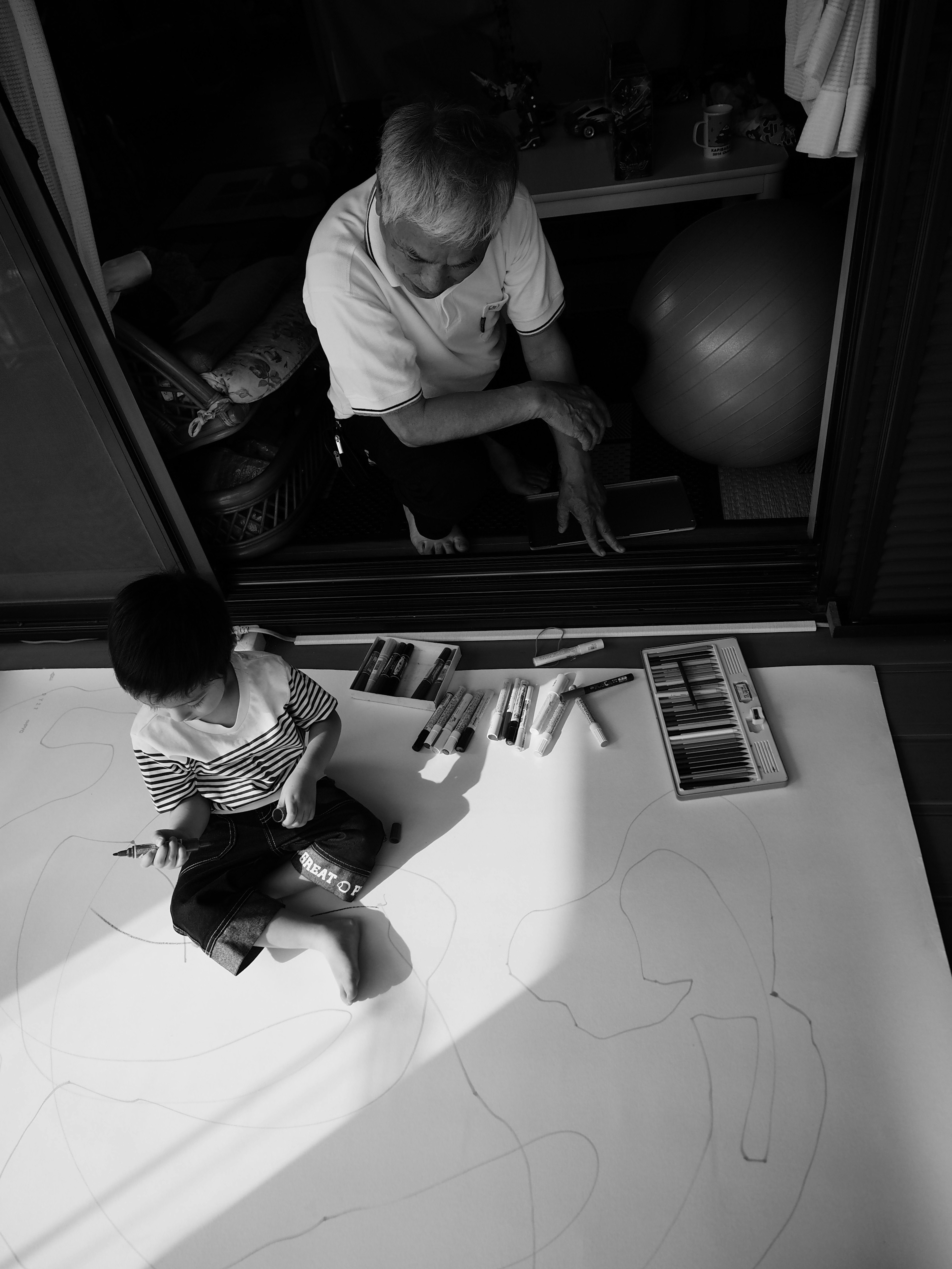 Un enfant assis par terre en train de dessiner avec des crayons tandis qu'un adulte observe à proximité