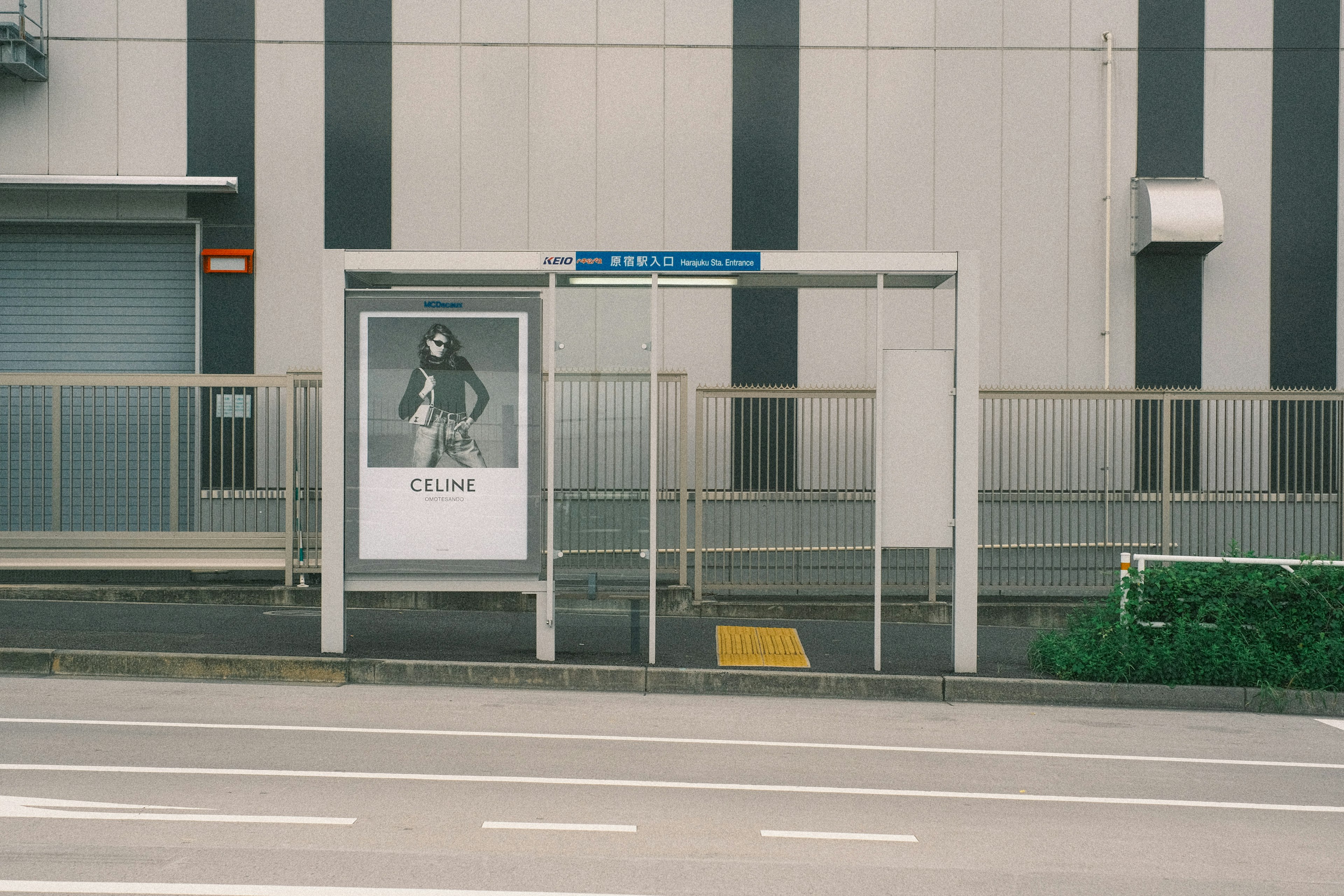 バス停に掲示されたモノクロ写真の広告と周囲の建物のデザイン