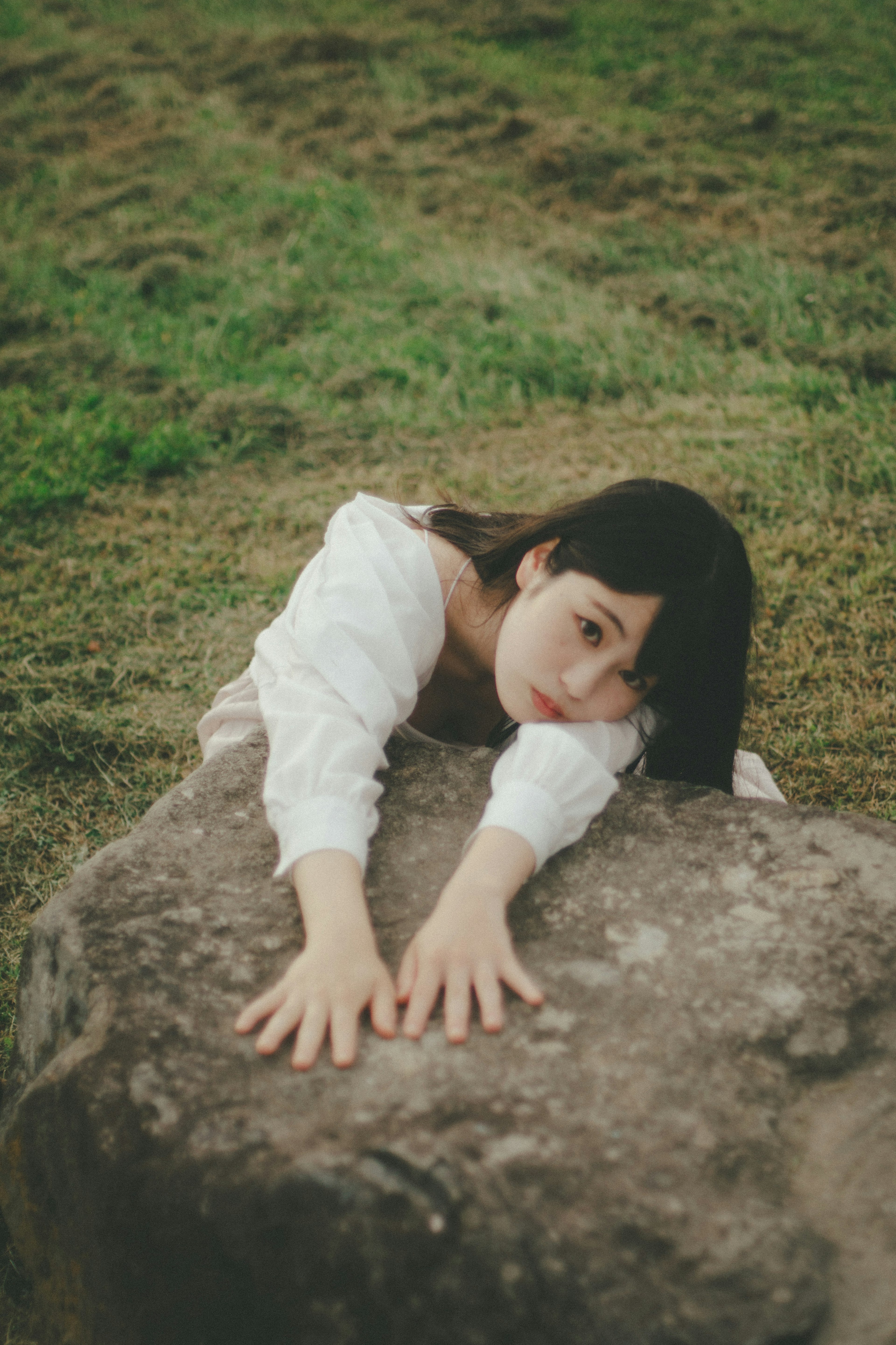 一位女性躺在草地上的一块石头上