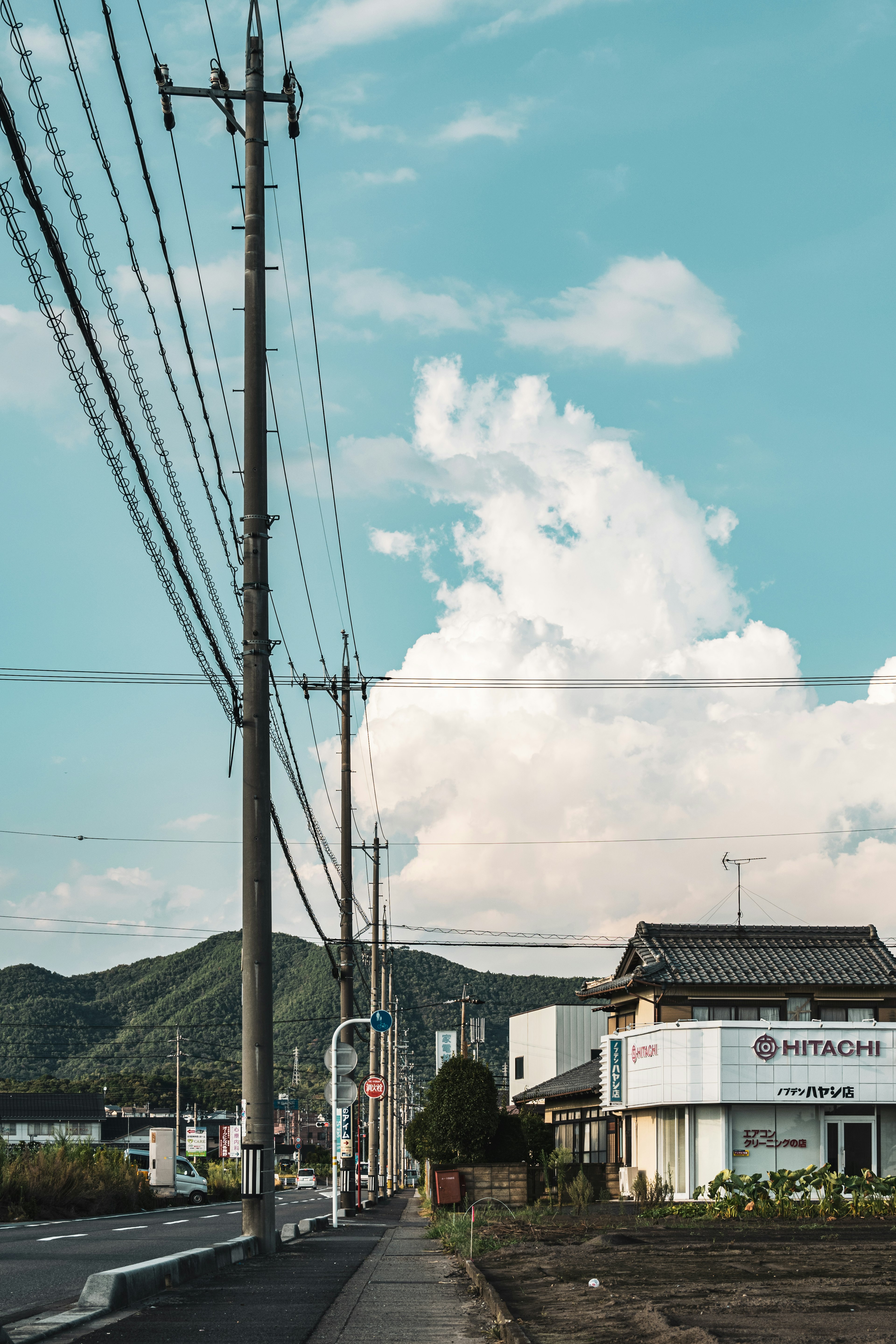 Street view featuring blue sky and white clouds with utility poles and a shop