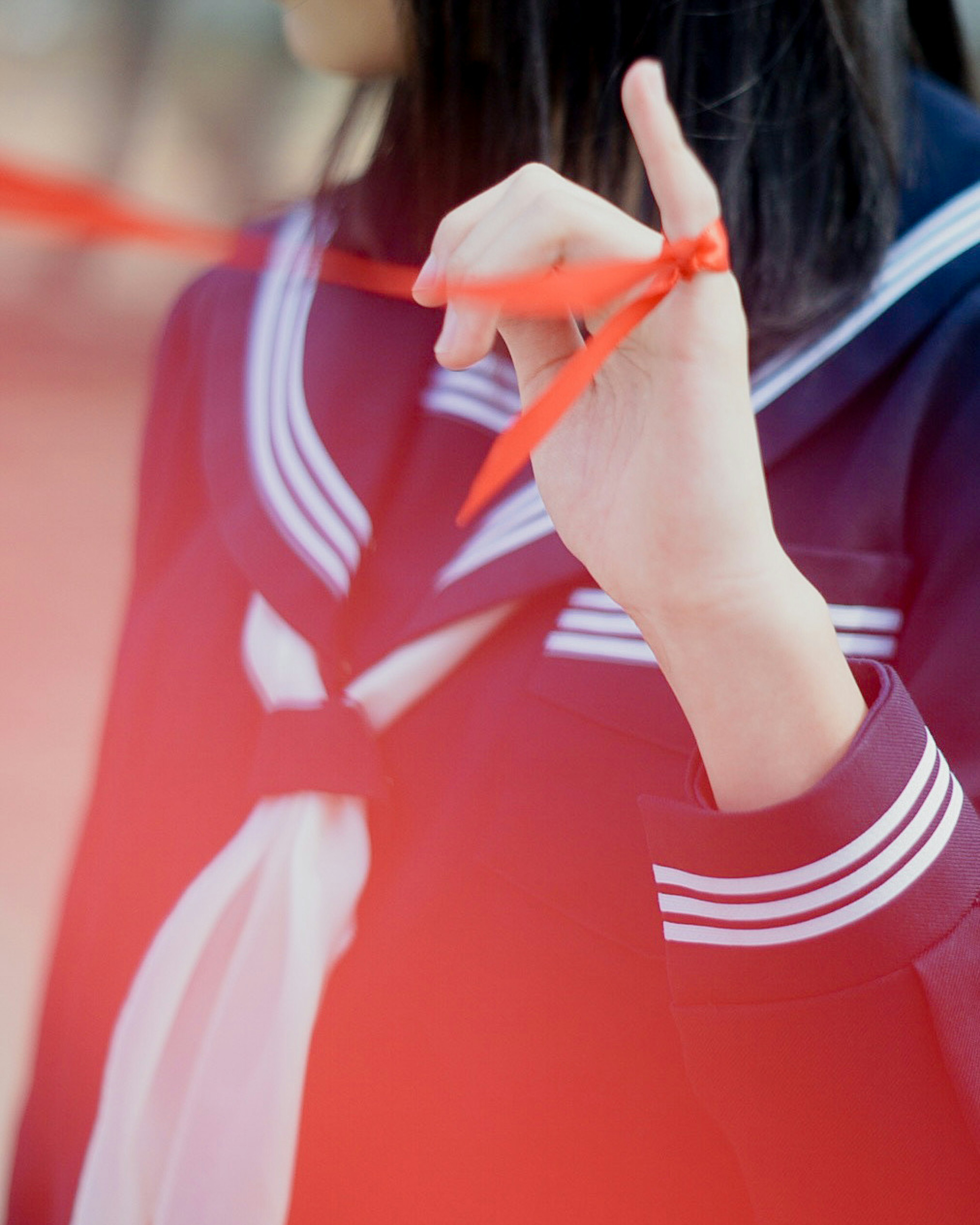 Mädchen in Schuluniform, das ein rotes Band um ihren Finger bindet