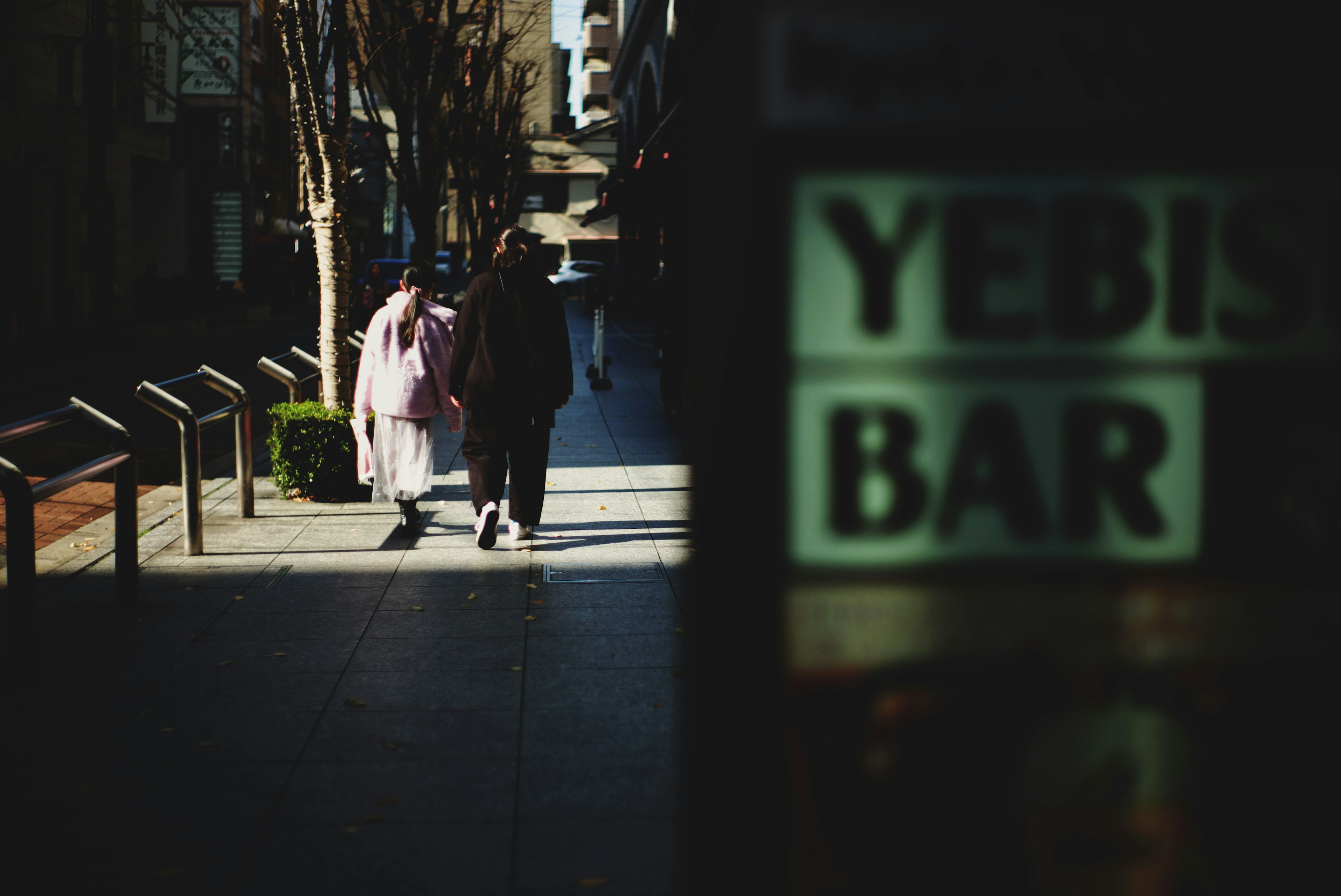 A scene of people walking on the street with a view of the YEBIS BAR sign