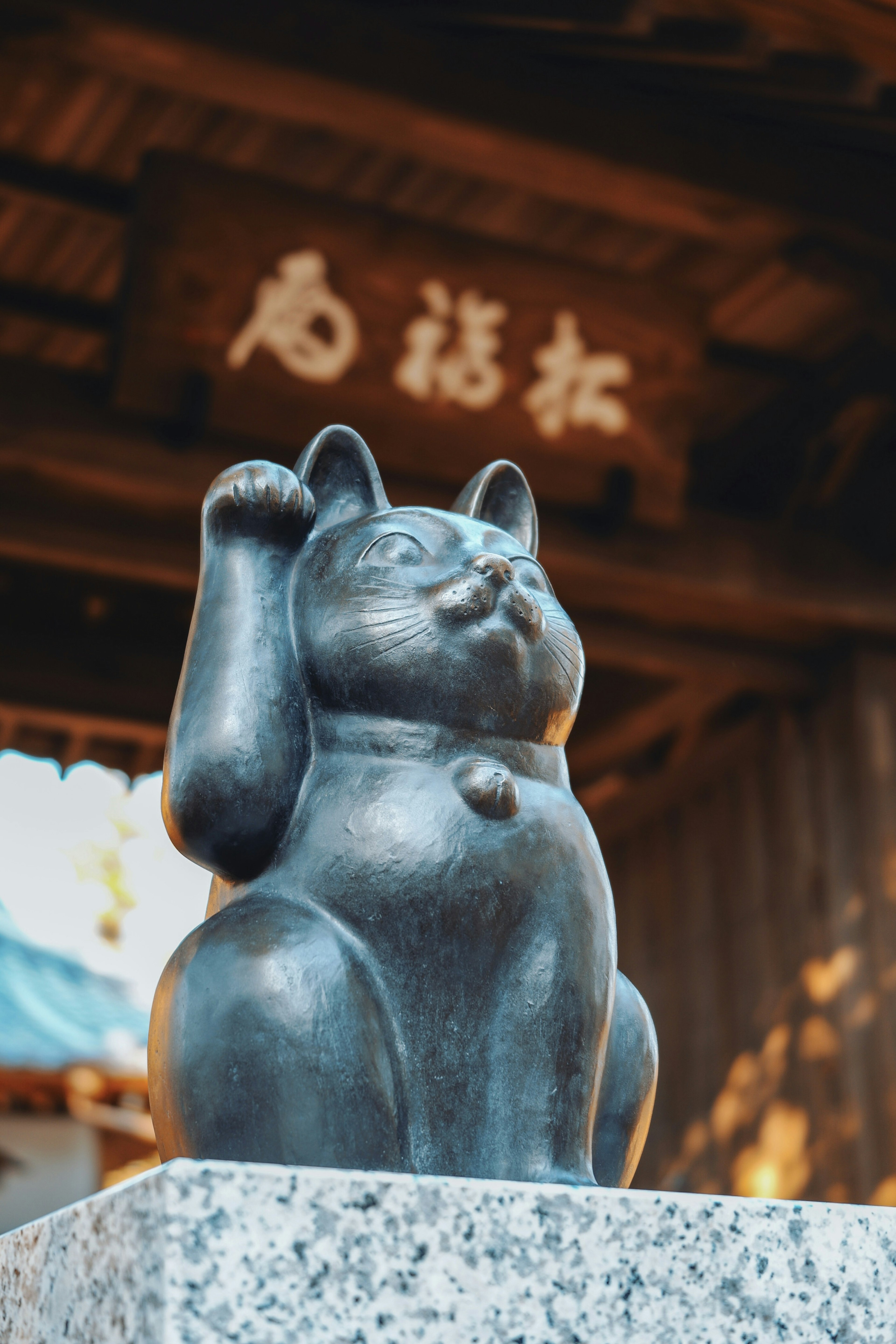 A black lucky cat statue on a stone pedestal