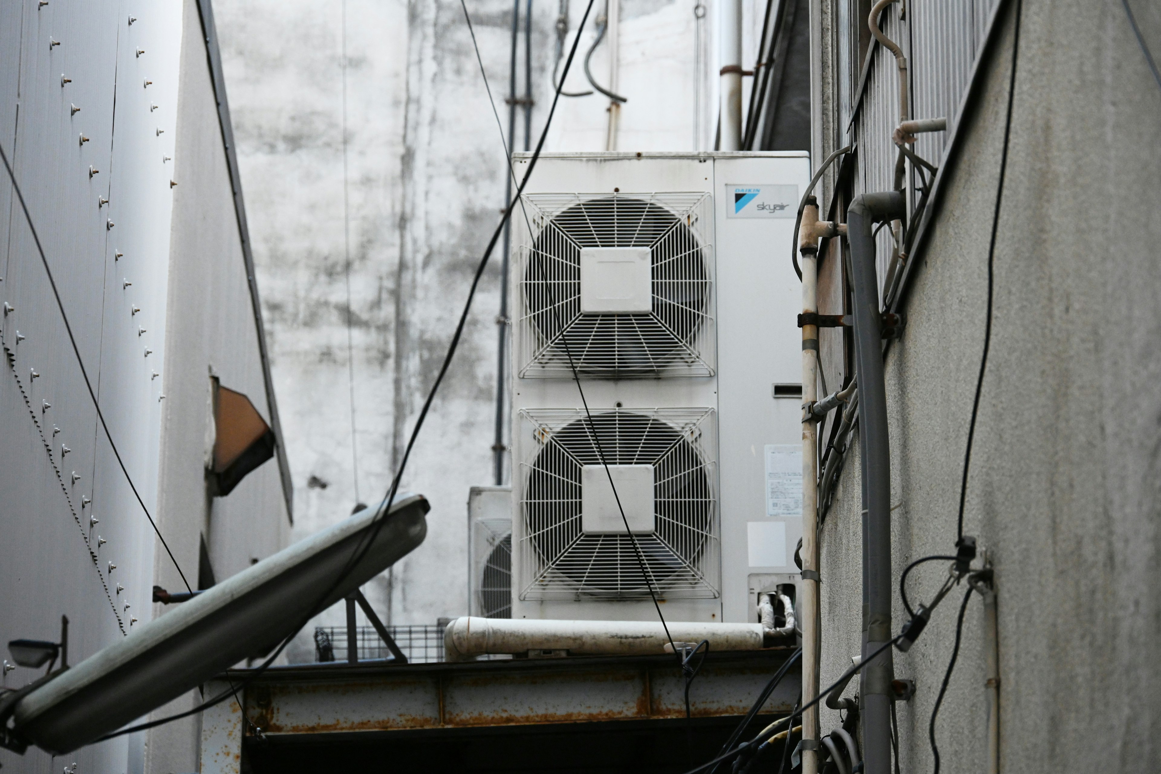 Two air conditioning units in a narrow alley with surrounding wires