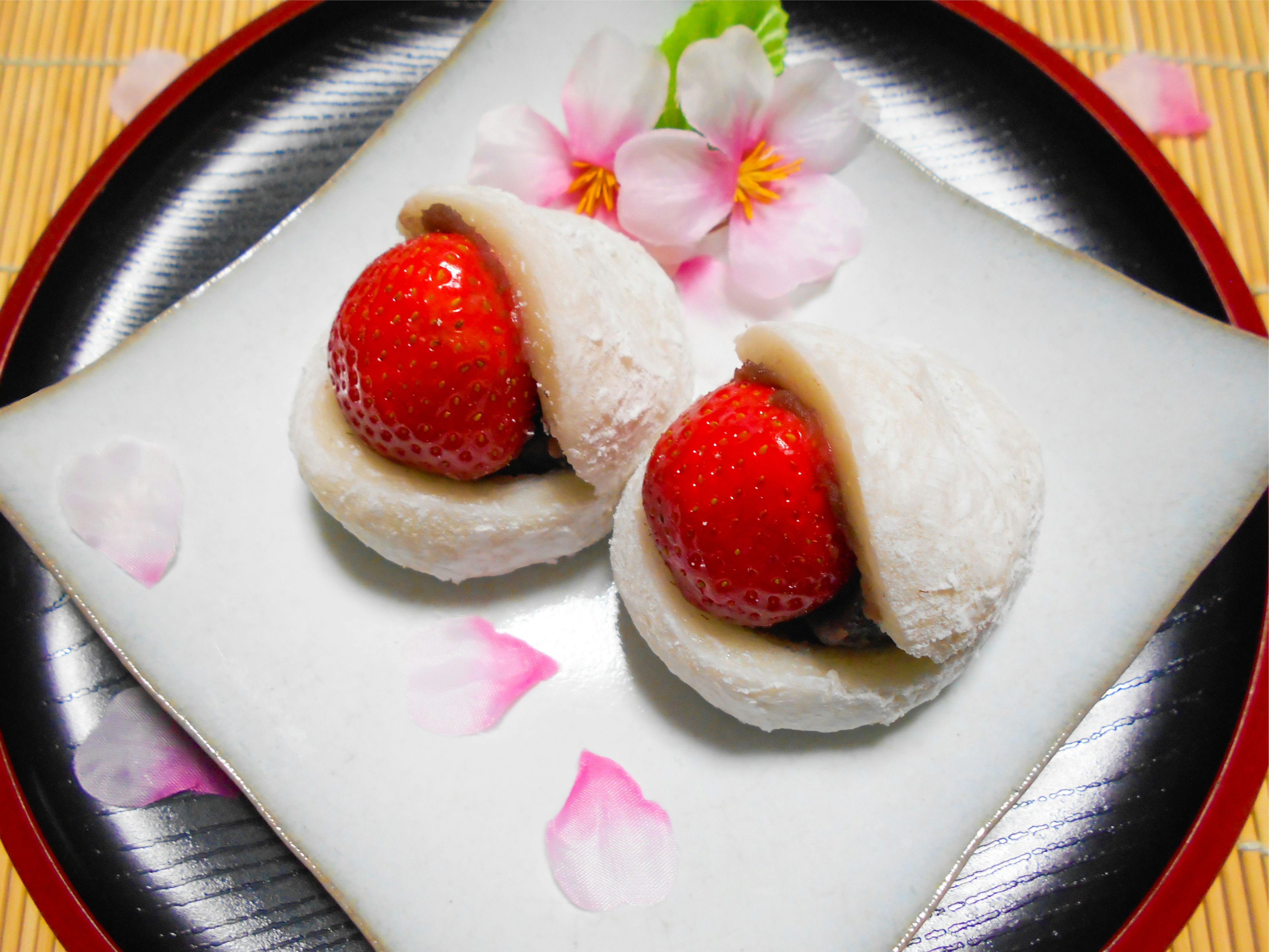 Two strawberry mochi on a decorative plate with flower petals