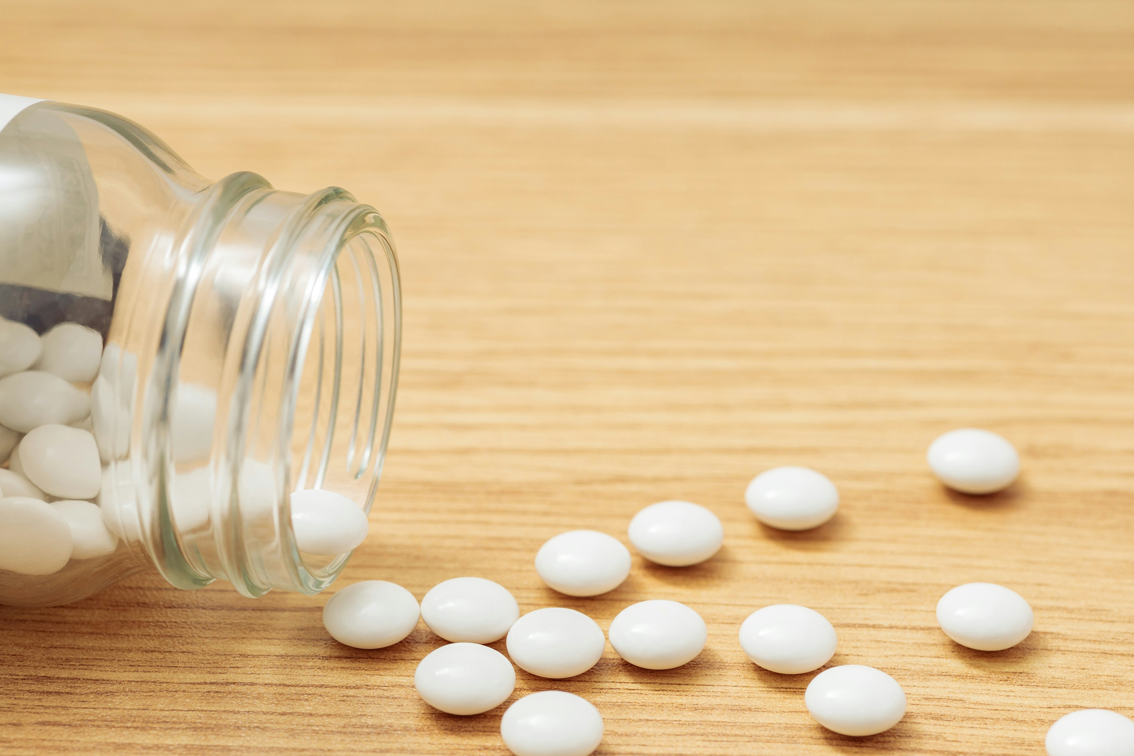 White pills scattered on a wooden surface from a glass jar