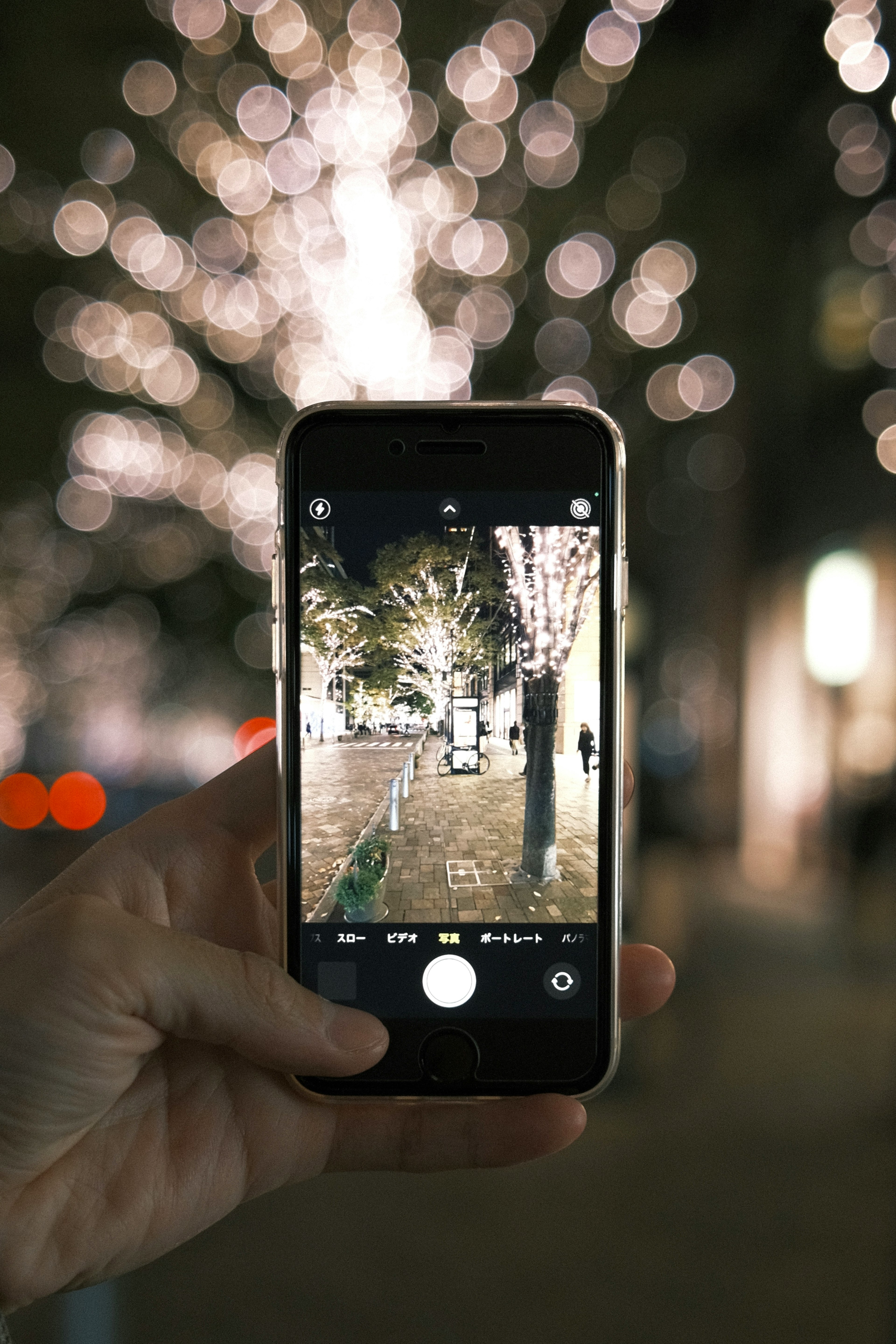 手に持たれたスマートフォンがイルミネーションを撮影している夜の風景