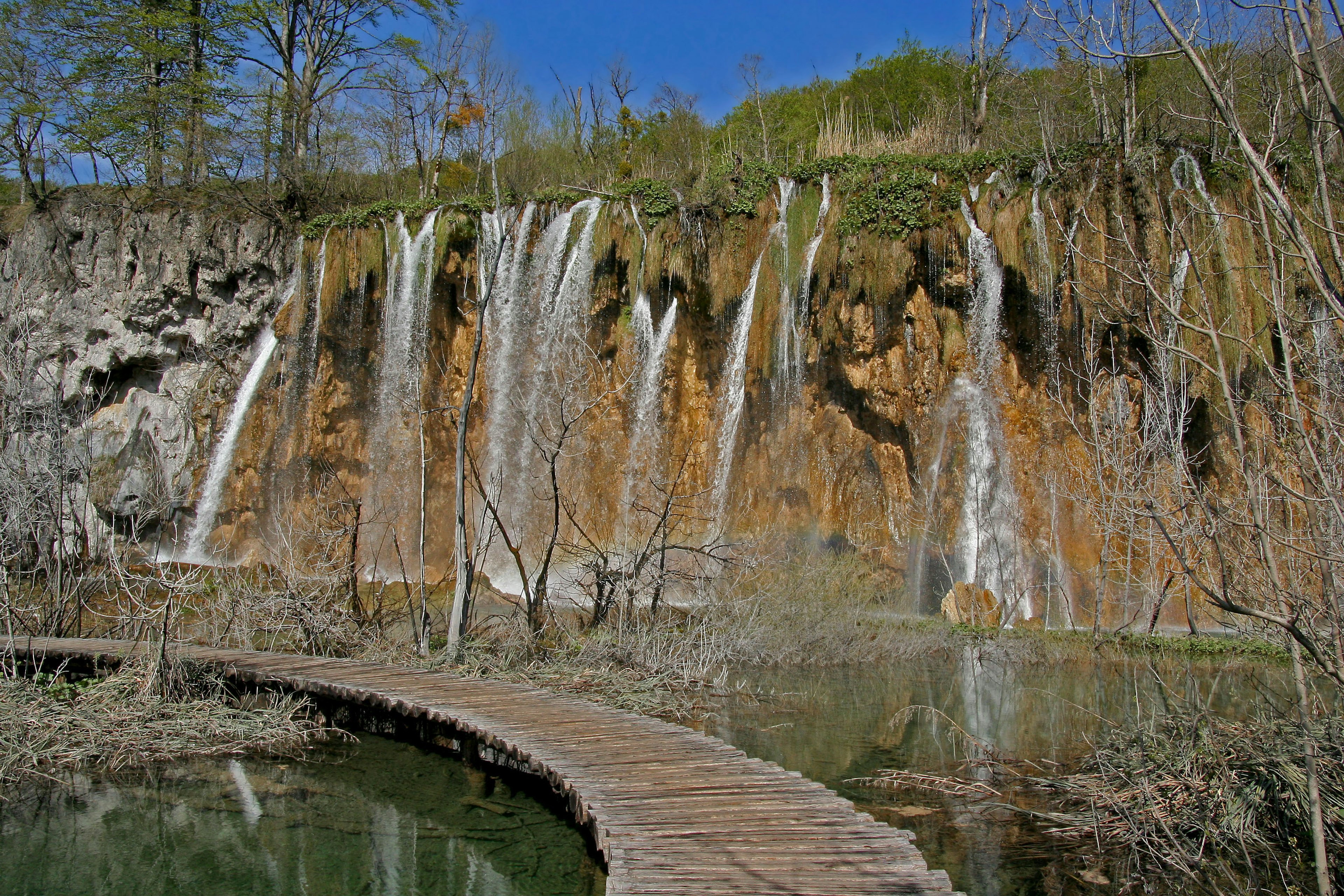 Vista panoramica di cascate che scorrono su una scogliera rocciosa con un sentiero di legno