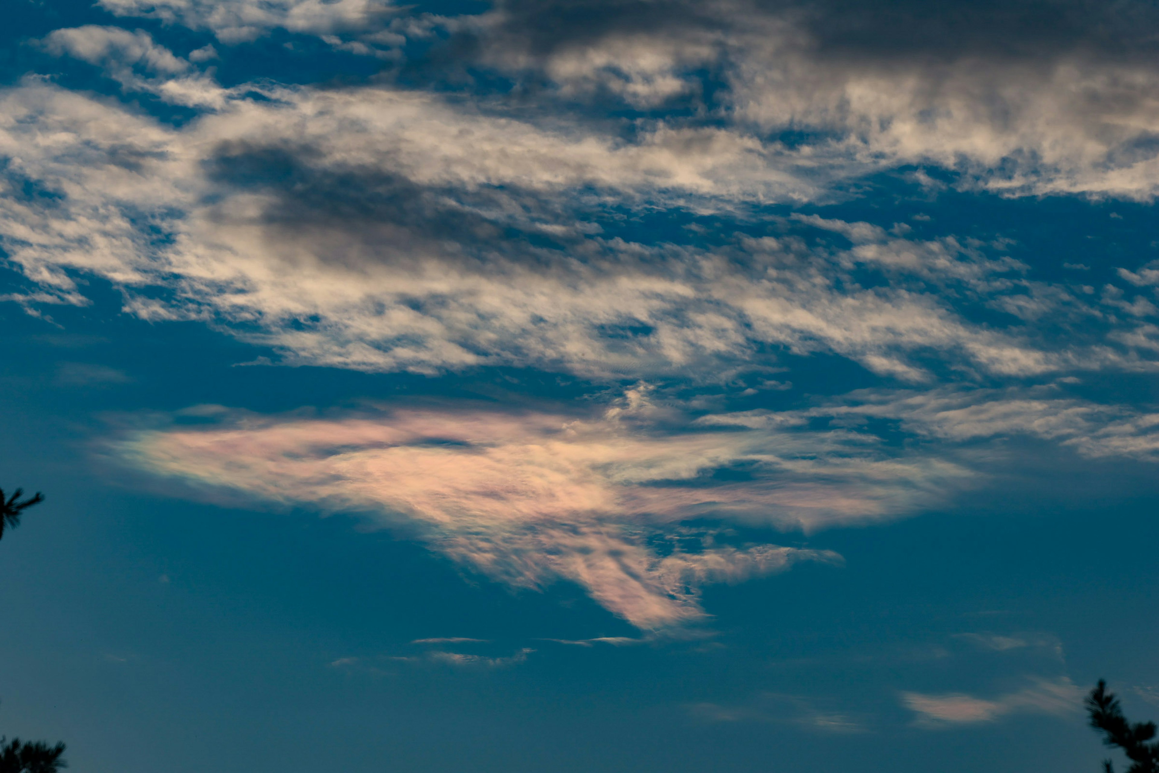 青い空に広がる雲と虹色の雲の形が特徴的な風景