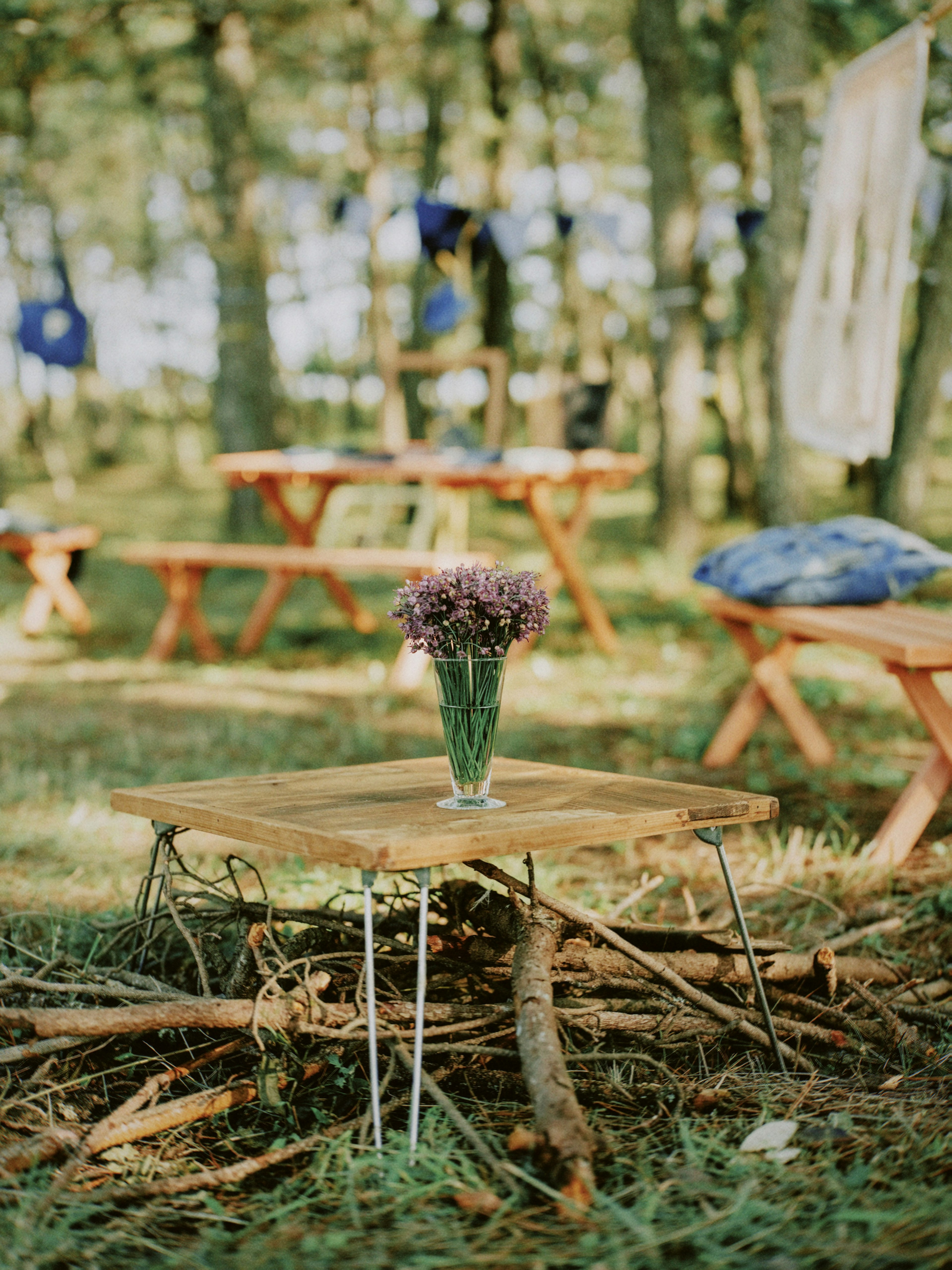 A small table in the woods with a vase of flowers on it