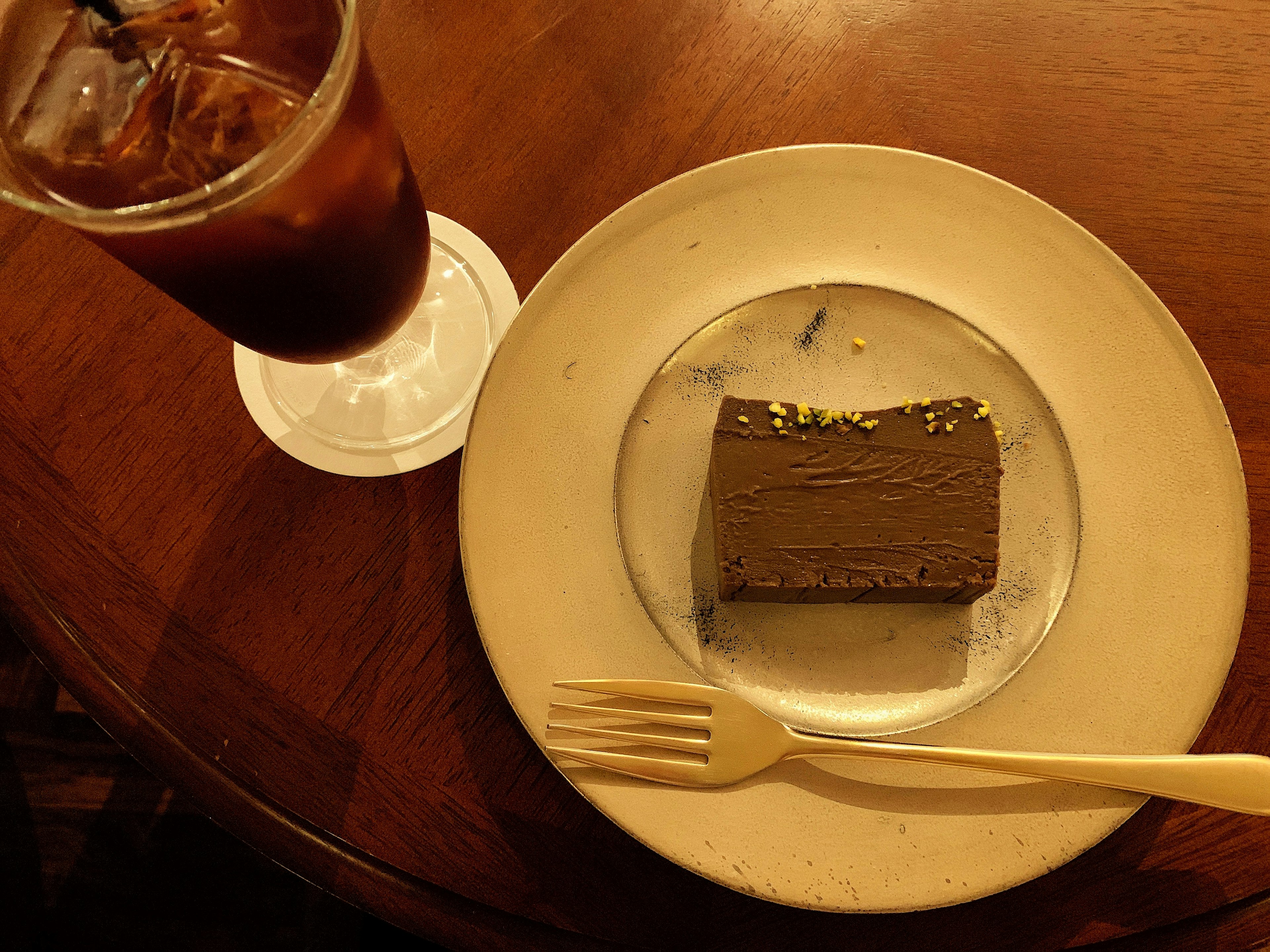 Chocolate cake on a plate with a fork and iced coffee in a glass