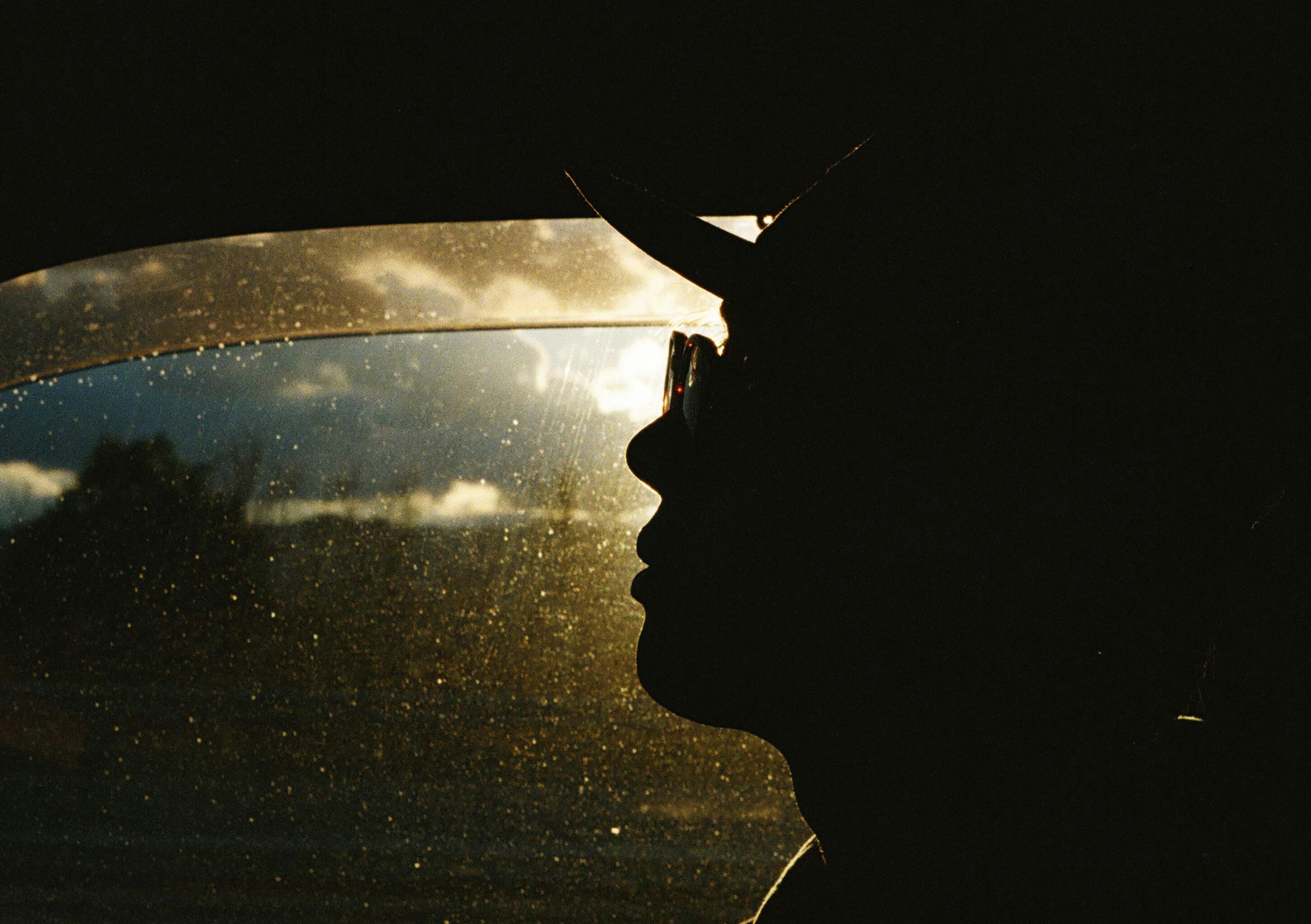 Silueta de una persona en un coche con reflejos de atardecer en la ventana