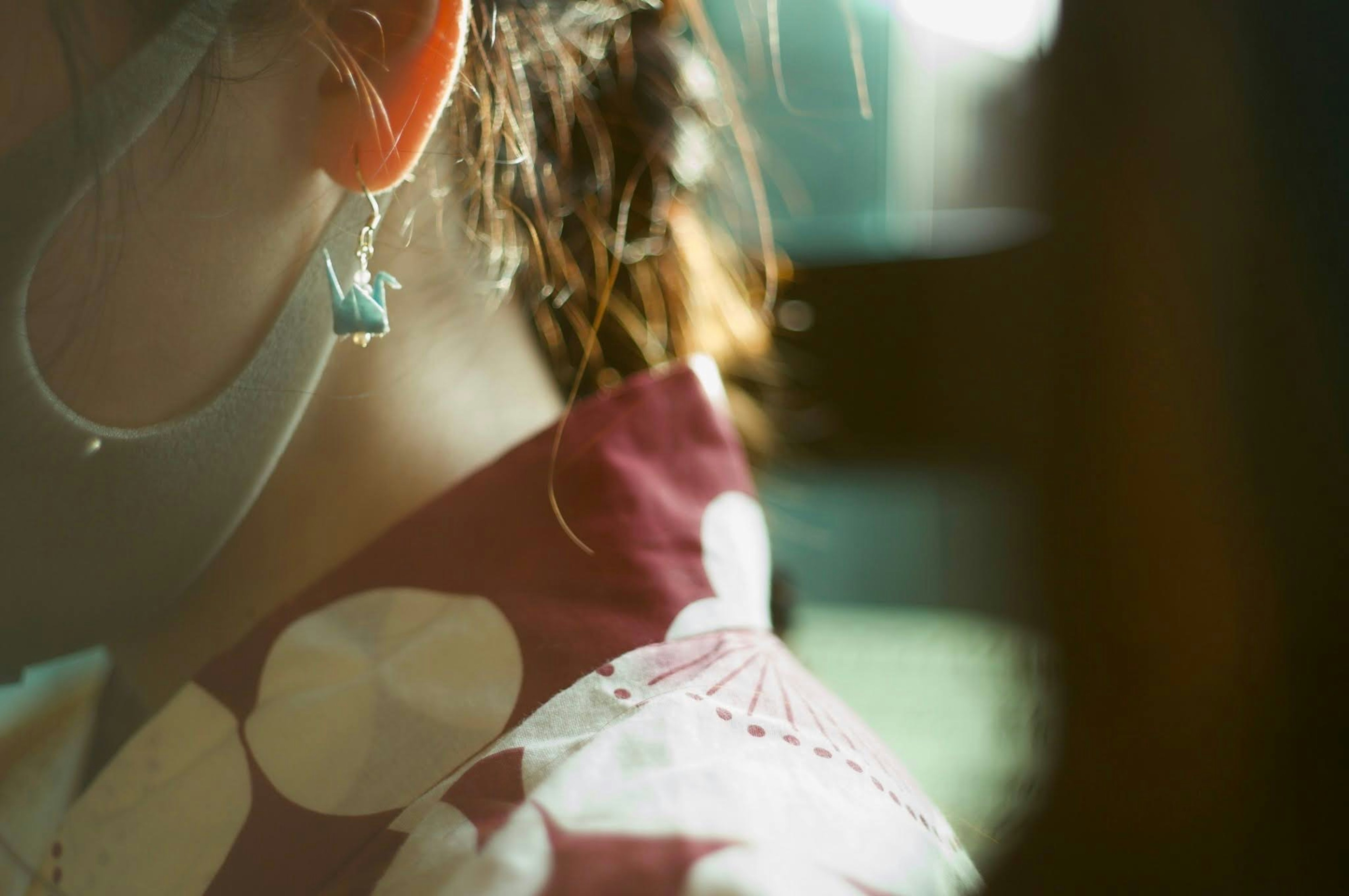 Gros plan sur l'oreille et les cheveux d'une femme avec un vêtement à motif rouge et des boucles d'oreilles bleues