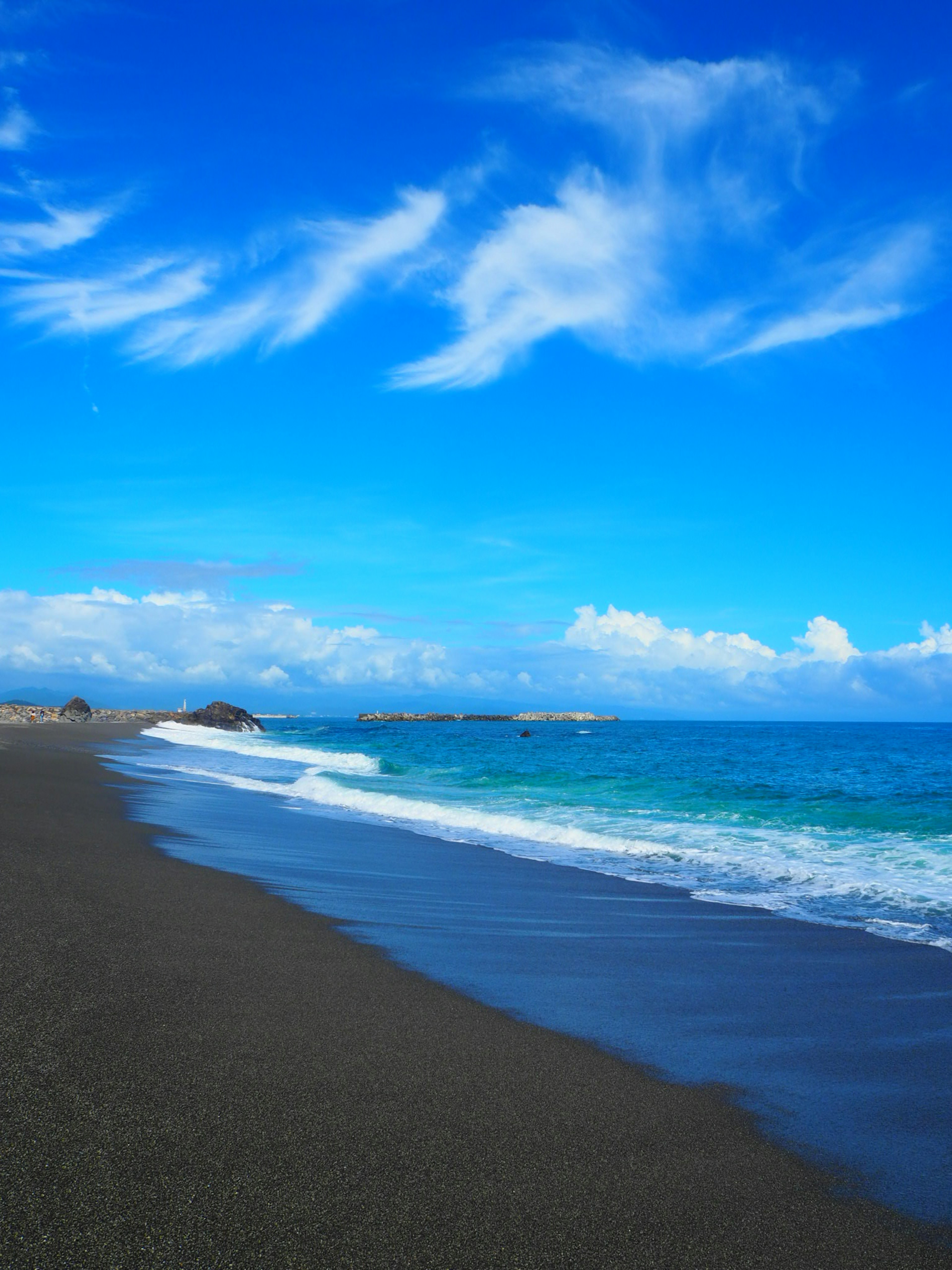 Playa de arena negra con océano azul bajo un cielo brillante y nubes blancas