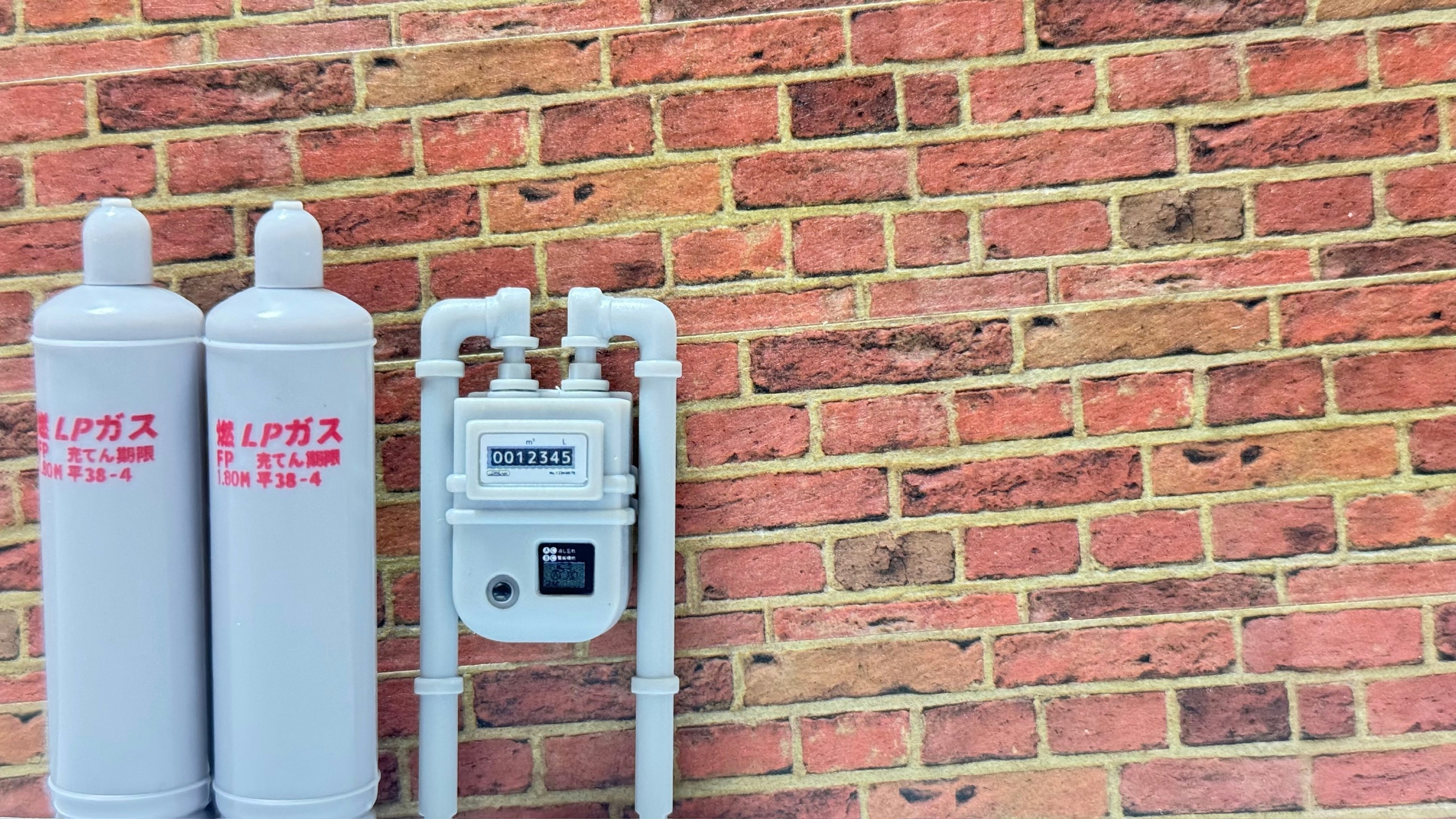 Two gas cylinders and a gas meter mounted on a red brick wall