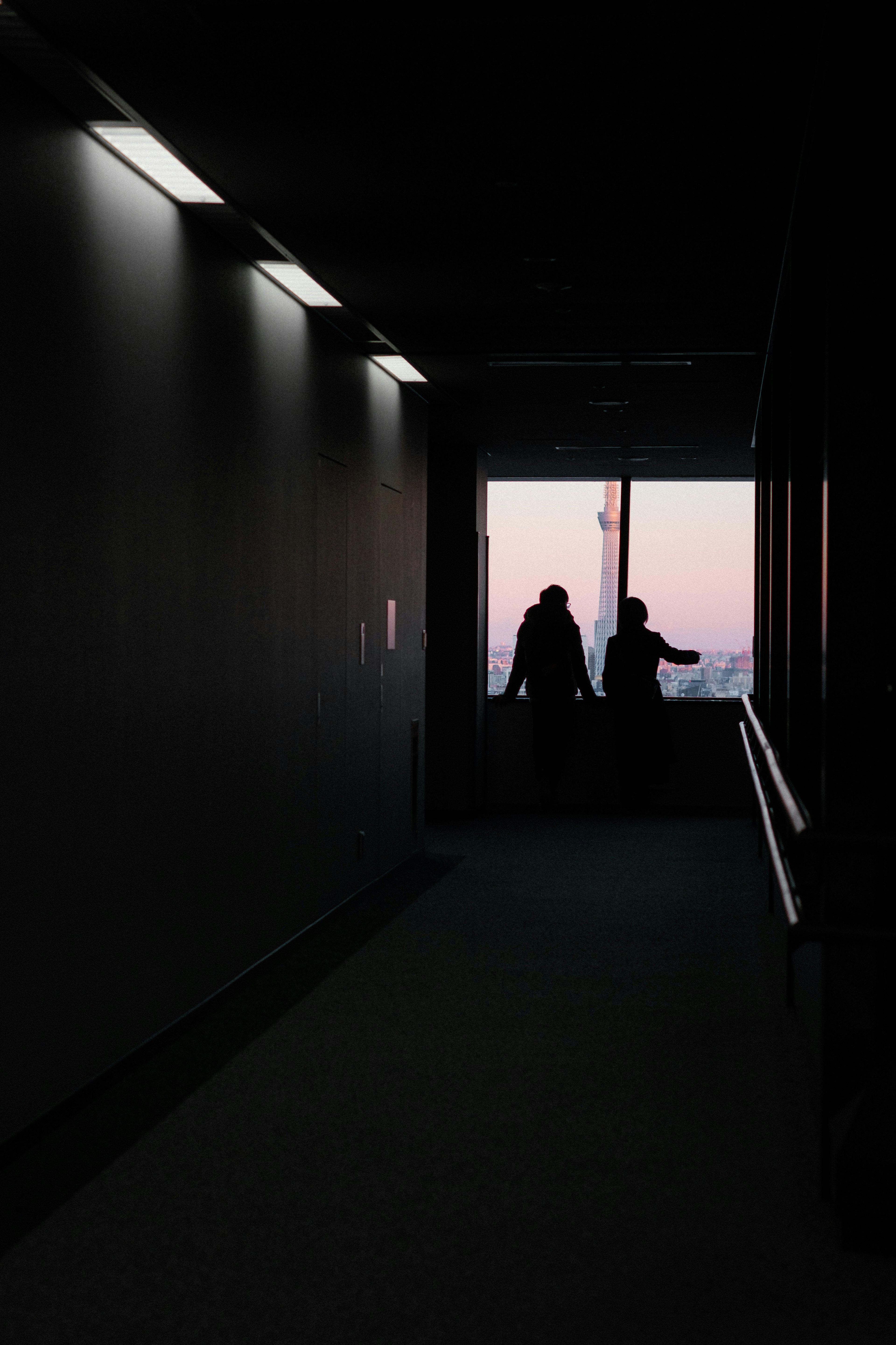 Silhouette von zwei Personen am Ende eines dunklen Flurs mit Blick auf den Sonnenuntergang draußen