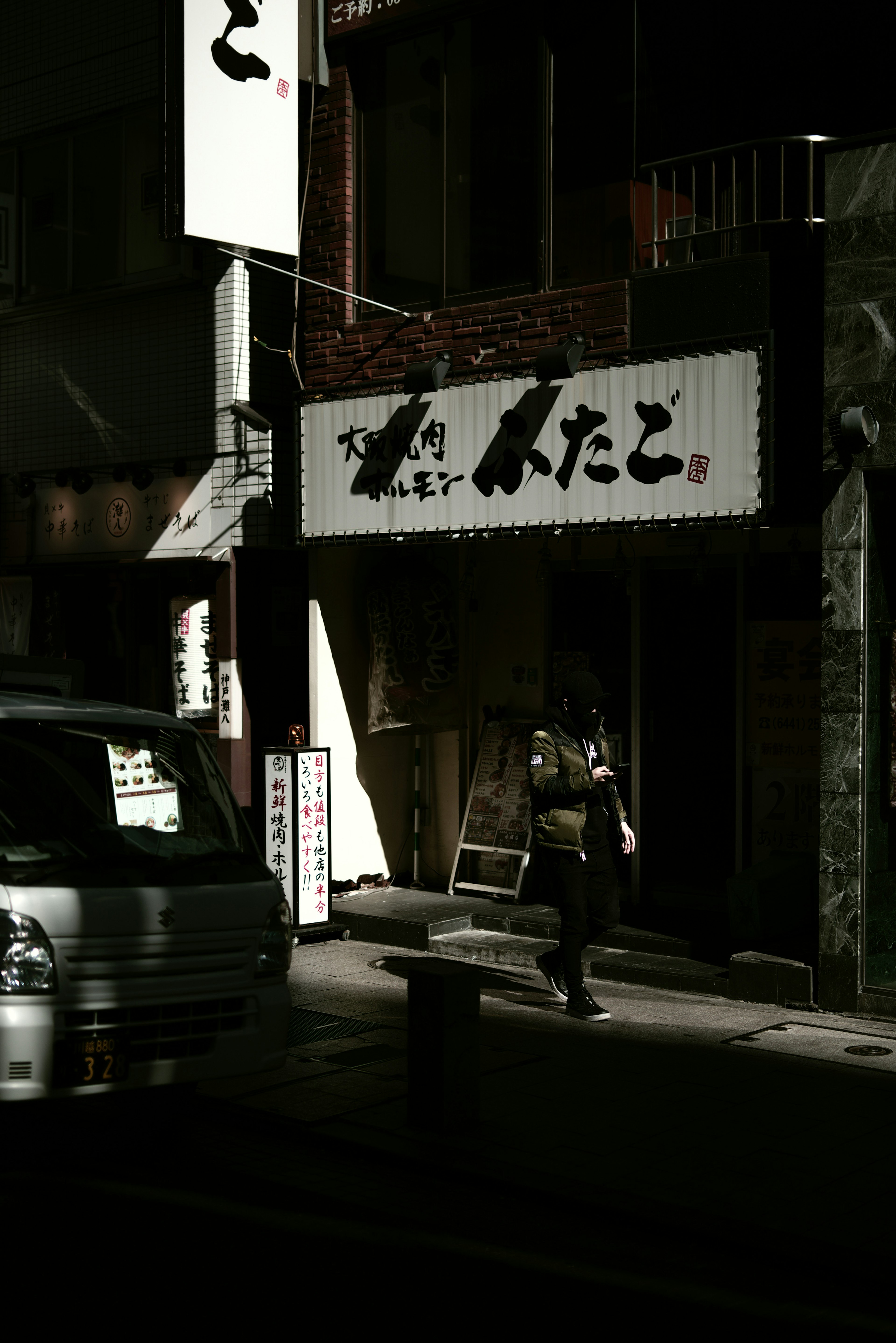 Silhouette d'une personne devant une enseigne de restaurant japonais dans une rue sombre