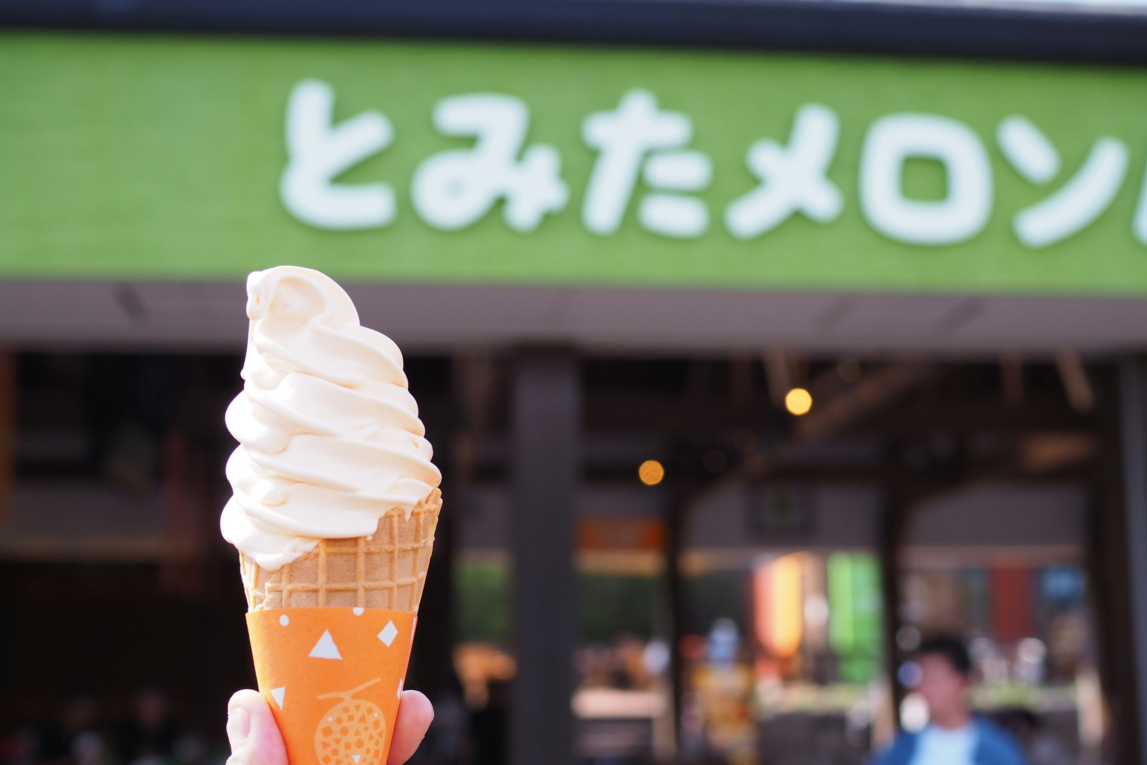 Hand holding soft serve ice cream with green sign in background