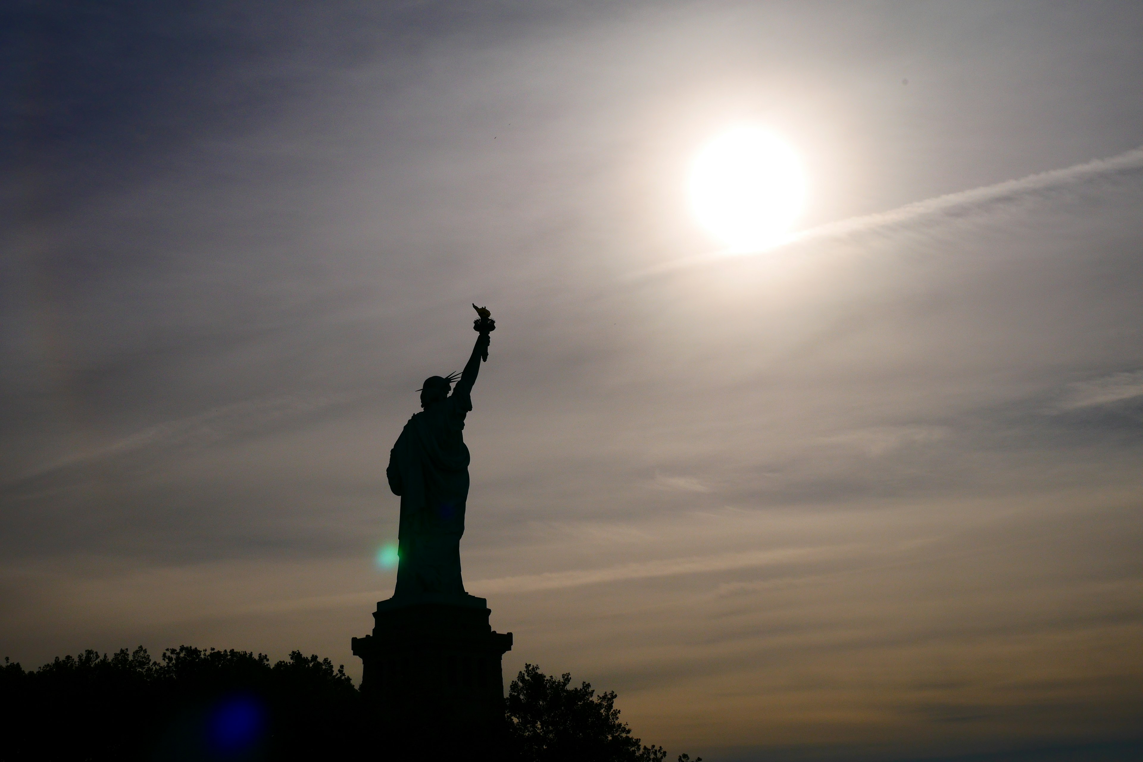 Silhouette of the Statue of Liberty against a bright sun