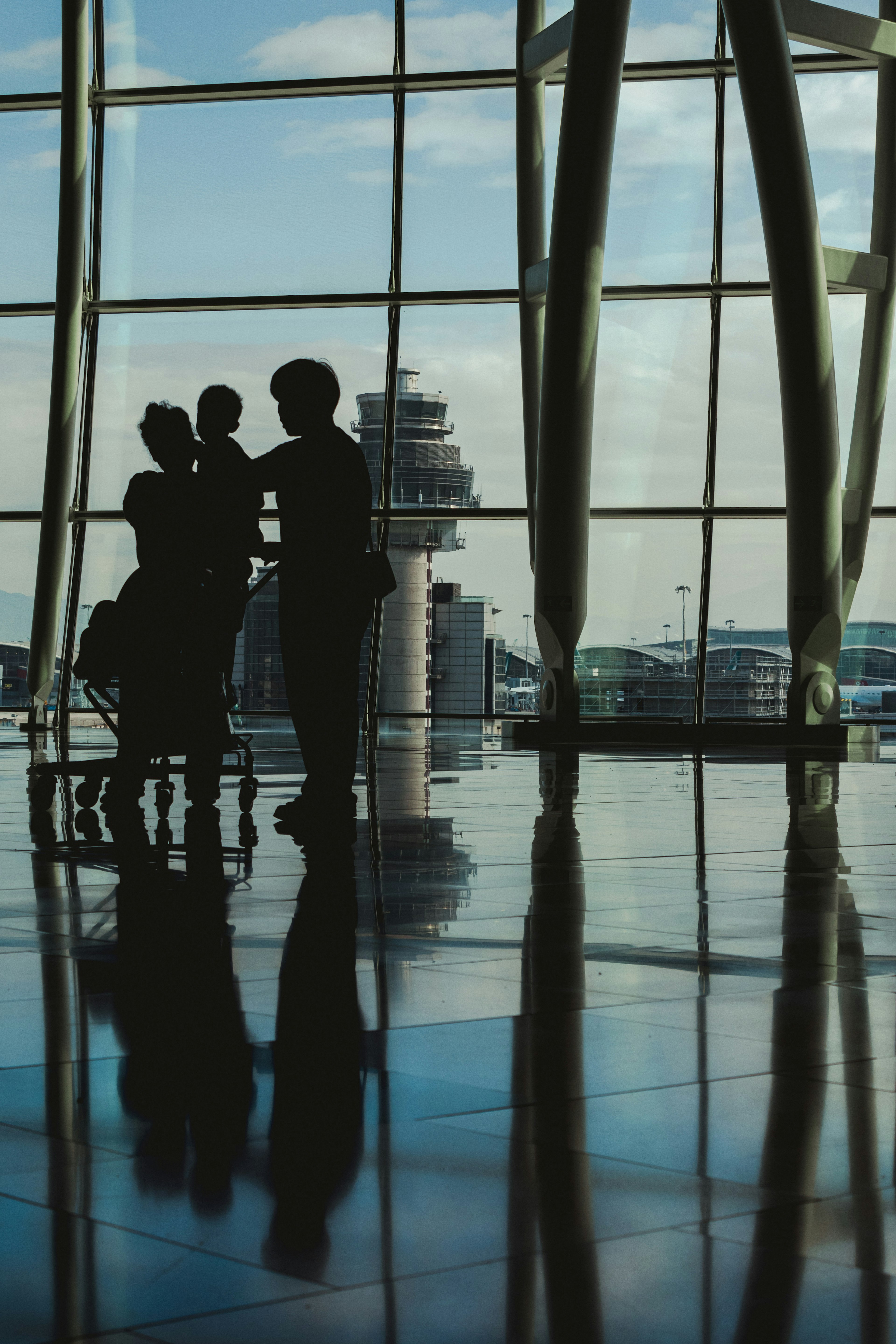 Siluetas de personas en un terminal de aeropuerto con una torre de control de fondo