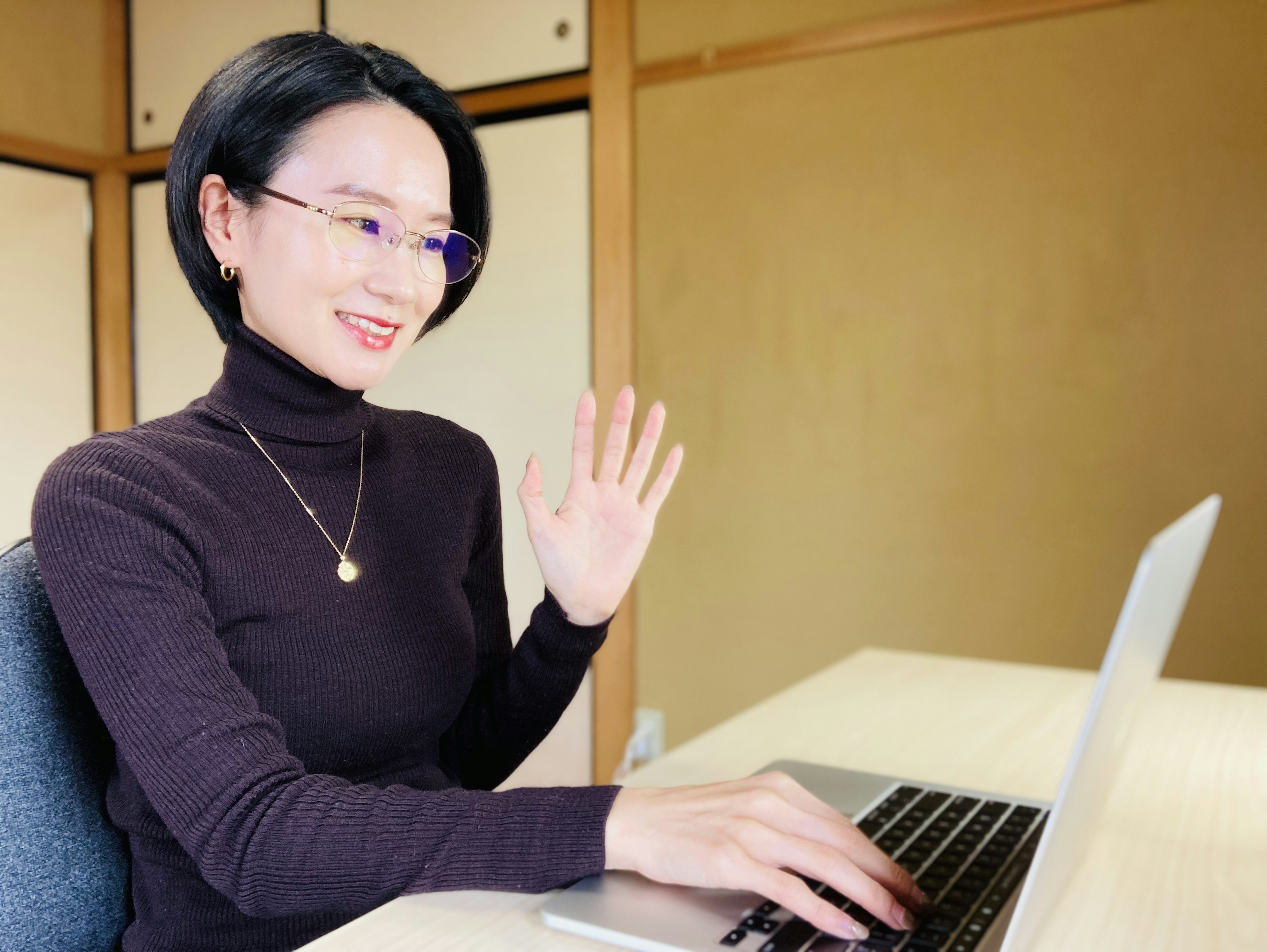 A woman smiling and waving while working on a laptop