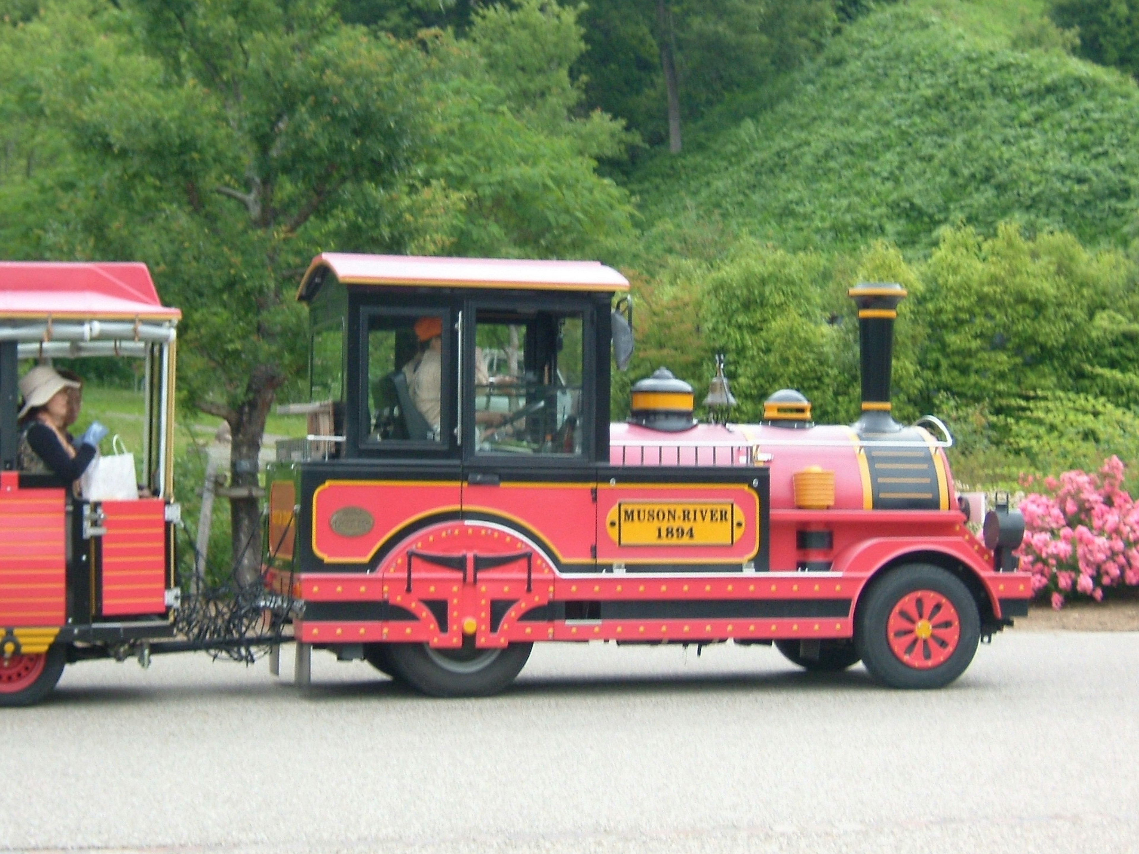 A colorful red miniature train traveling through a scenic landscape