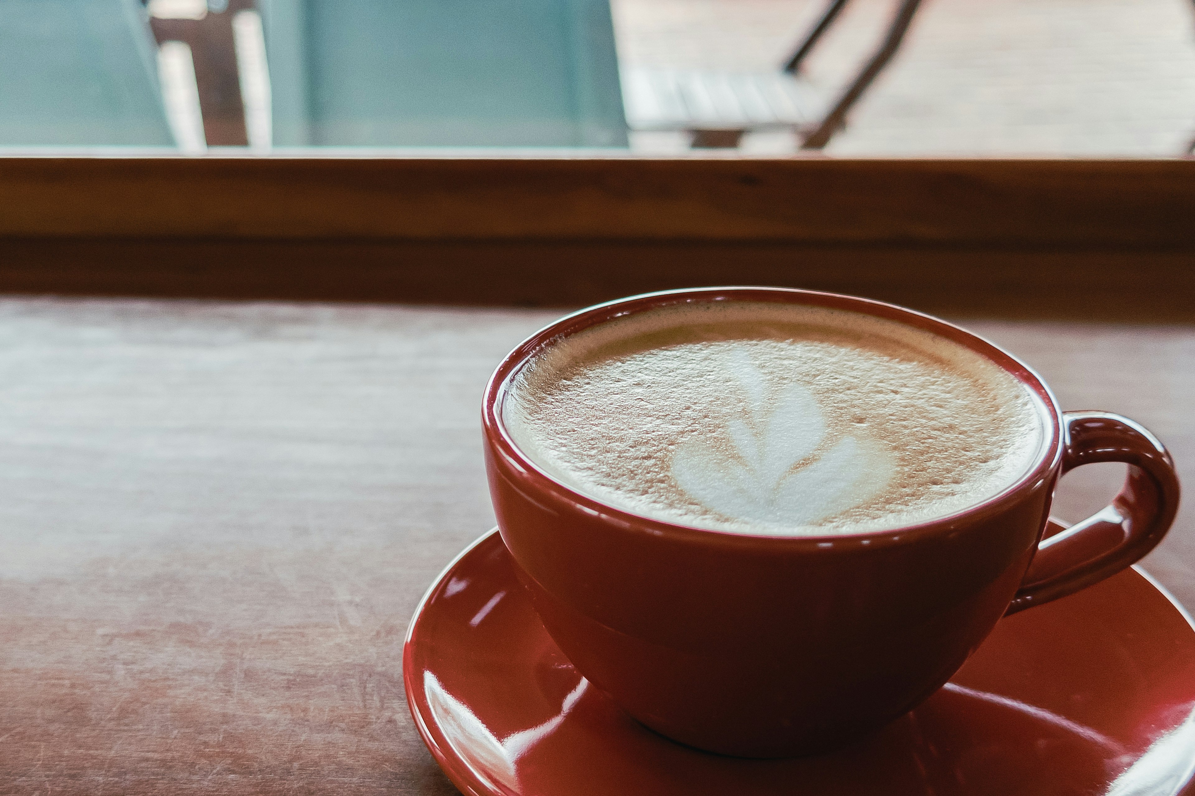 Kopi dalam cangkir merah dengan seni latte diletakkan di atas meja kayu