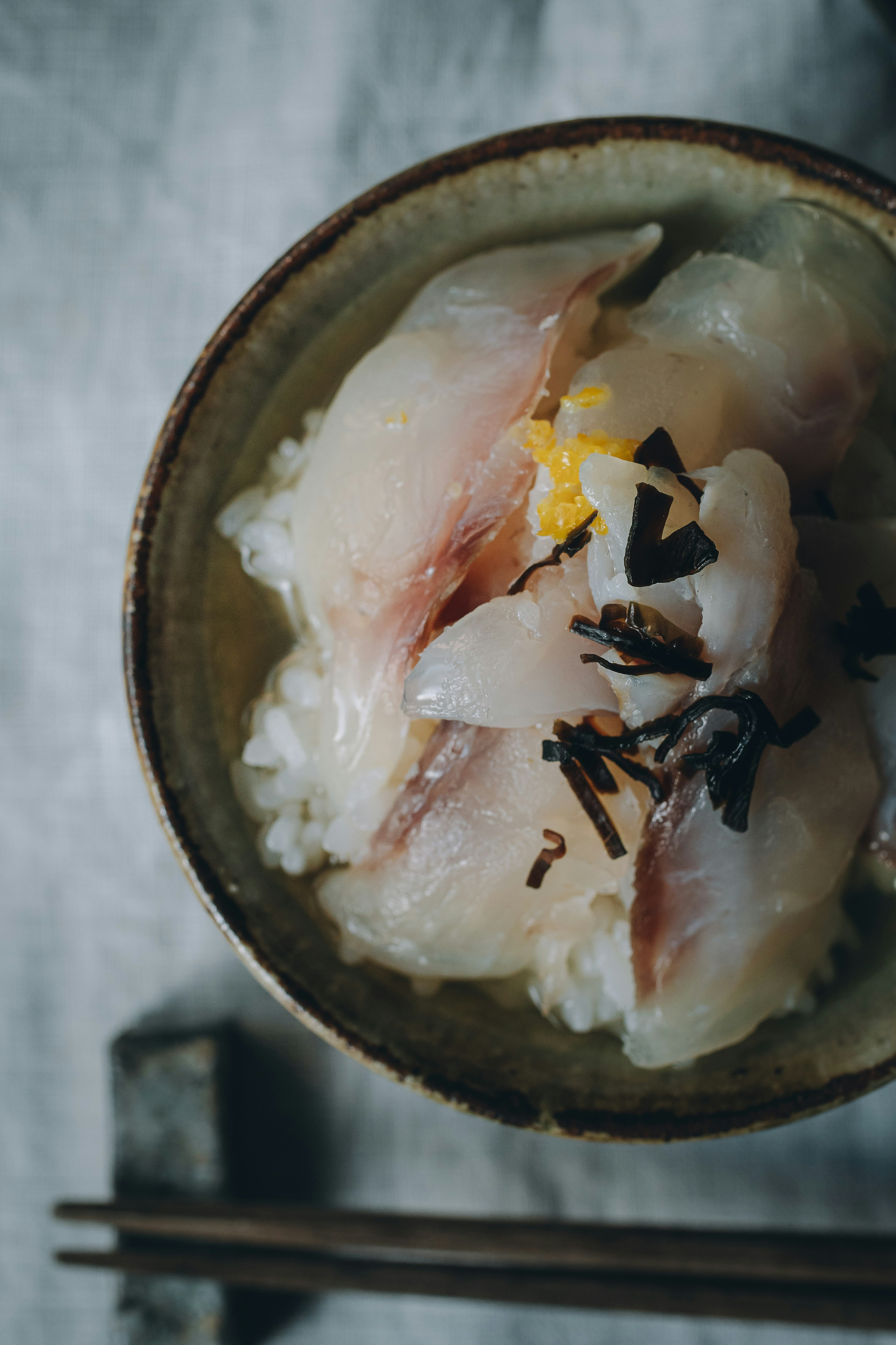 Tazón de arroz sushi cubierto con sashimi fresco y guarniciones de algas