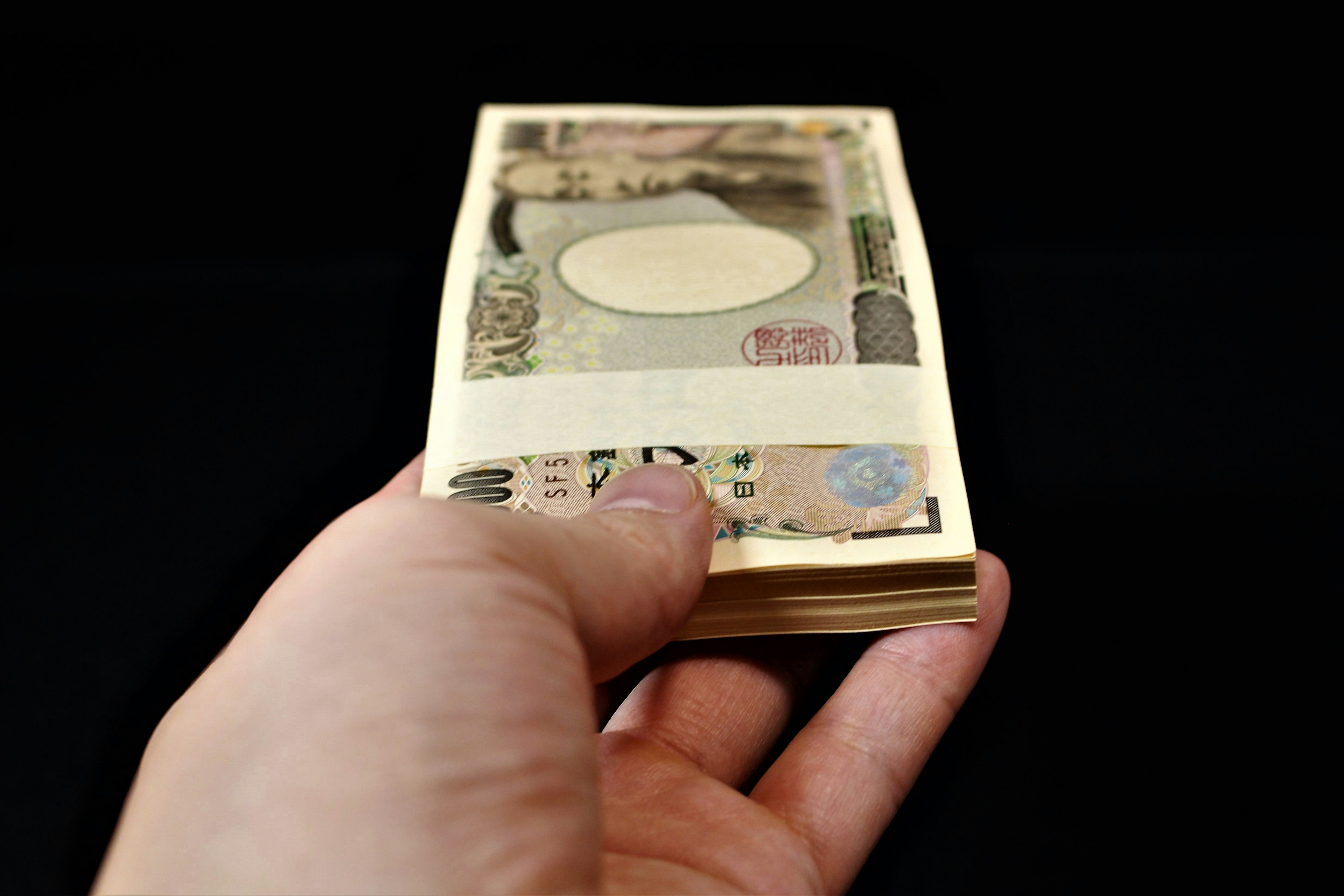 A hand holding a bundle of Japanese banknotes against a black background