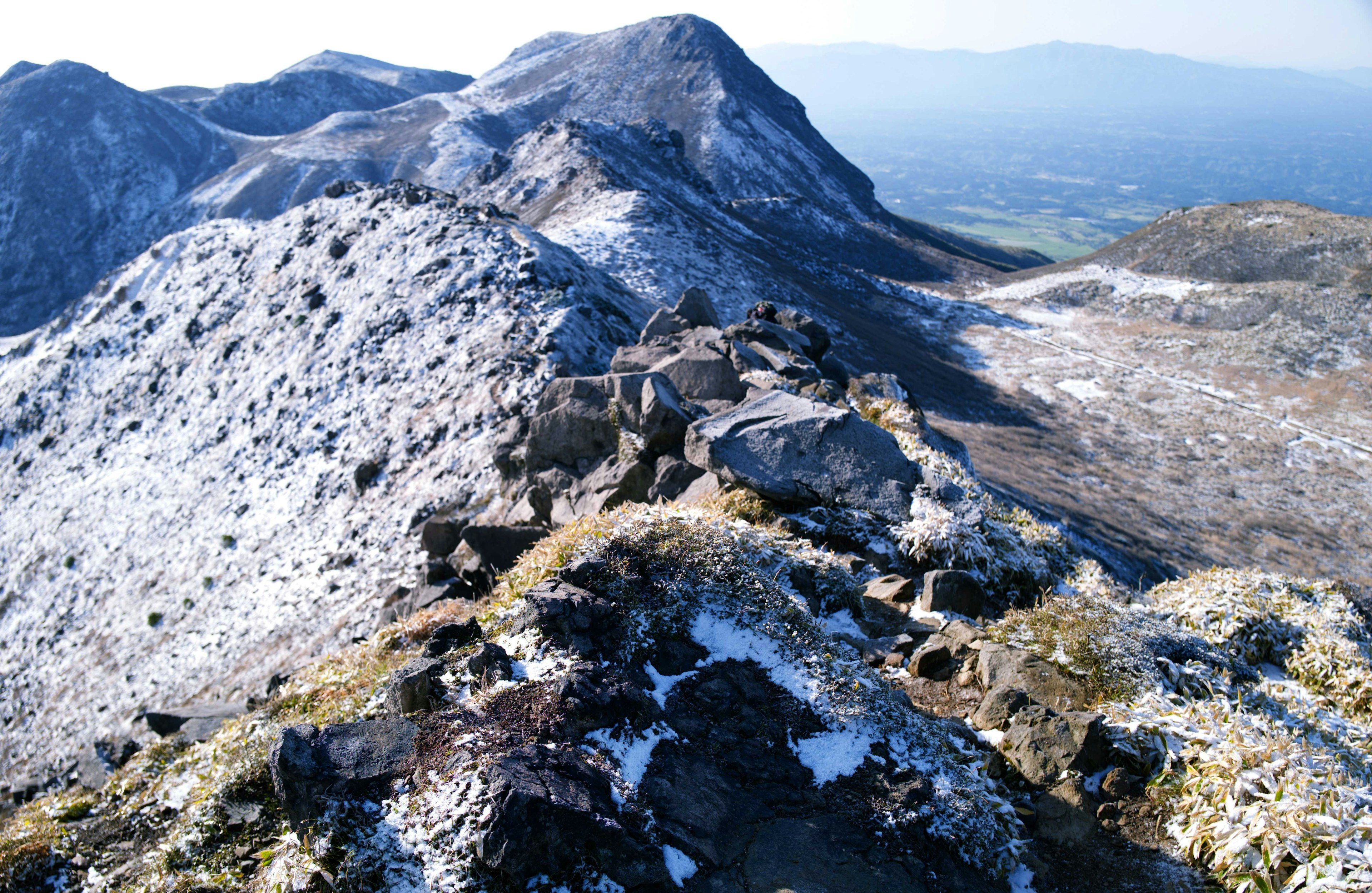 View from the snowy mountain peak overlooking green valleys and a blue sky