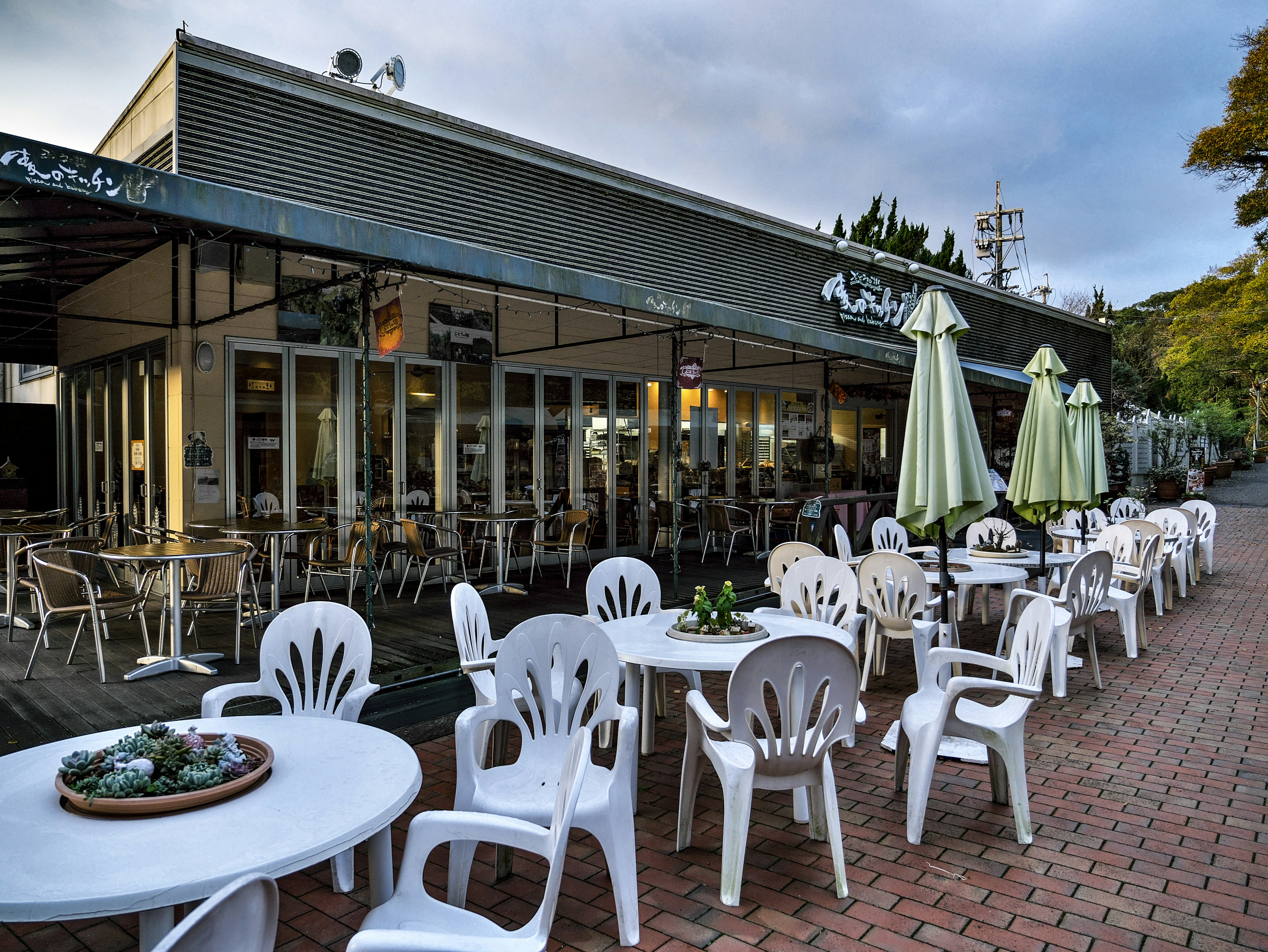 Exterior de un café con asientos en terraza y sillas de plástico blancas