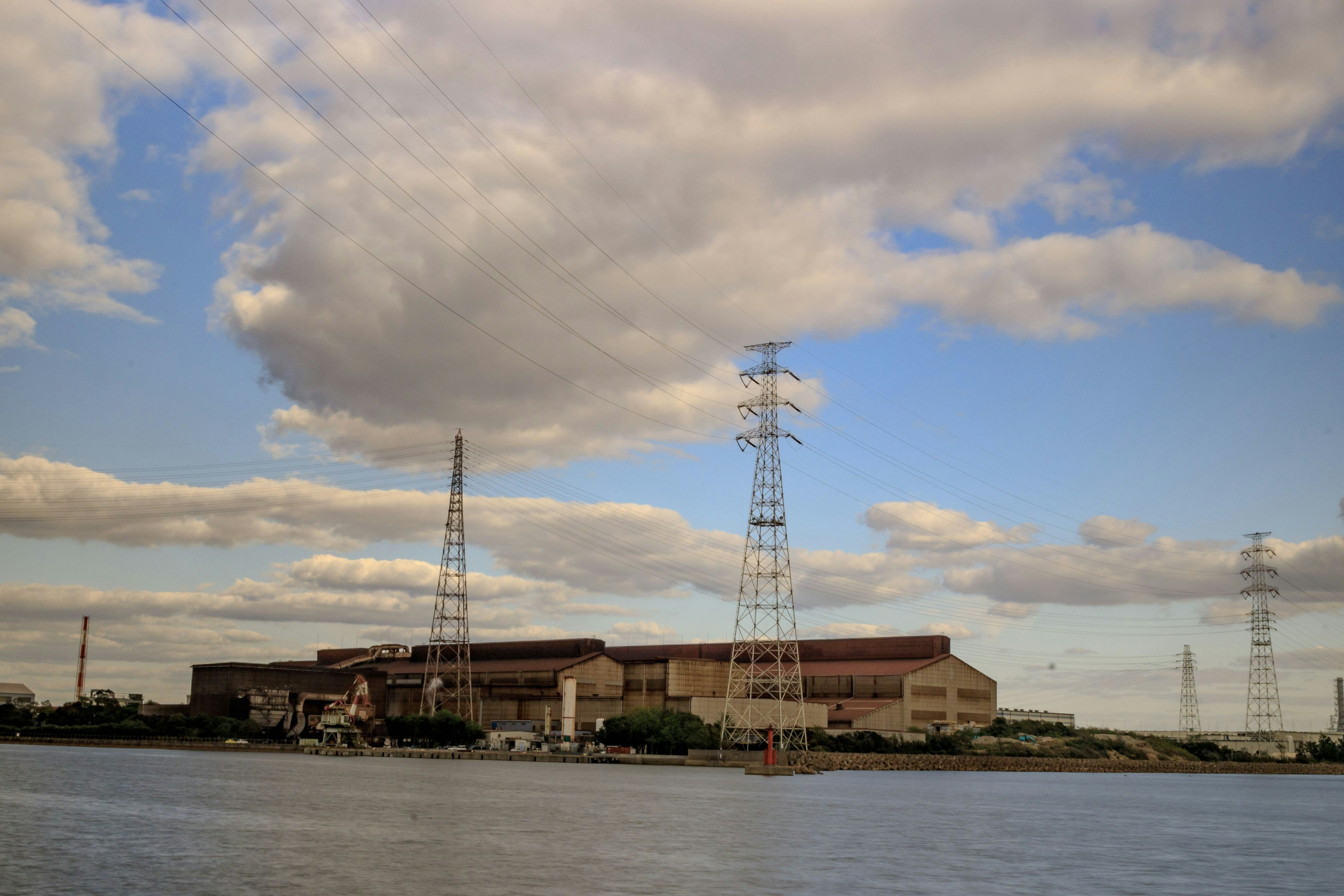 Fabbrica e linee elettriche dall'altra parte del fiume sotto un cielo nuvoloso