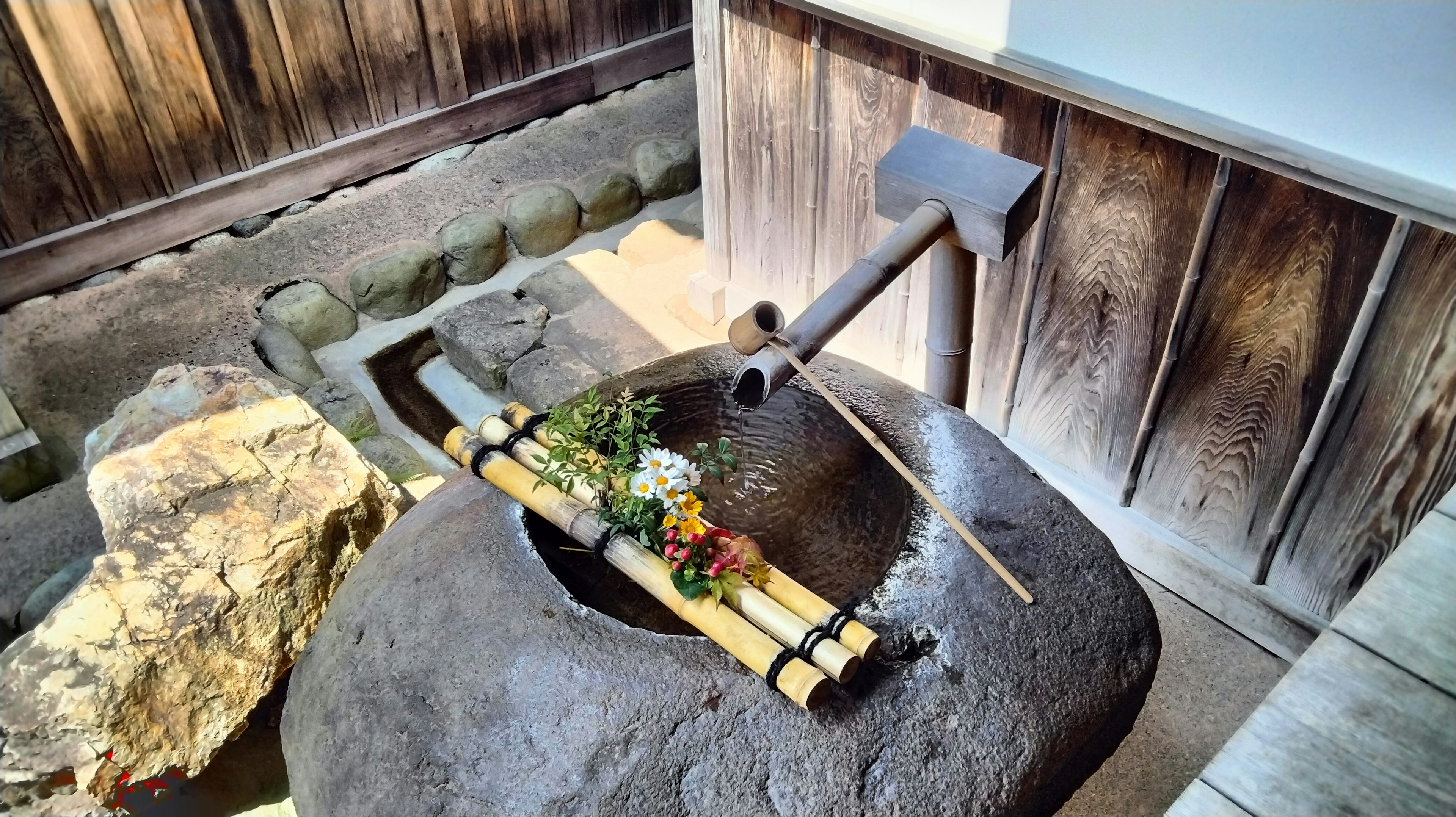 Elemento de jardín japonés con un estanque de piedra decorado con bambú y flores