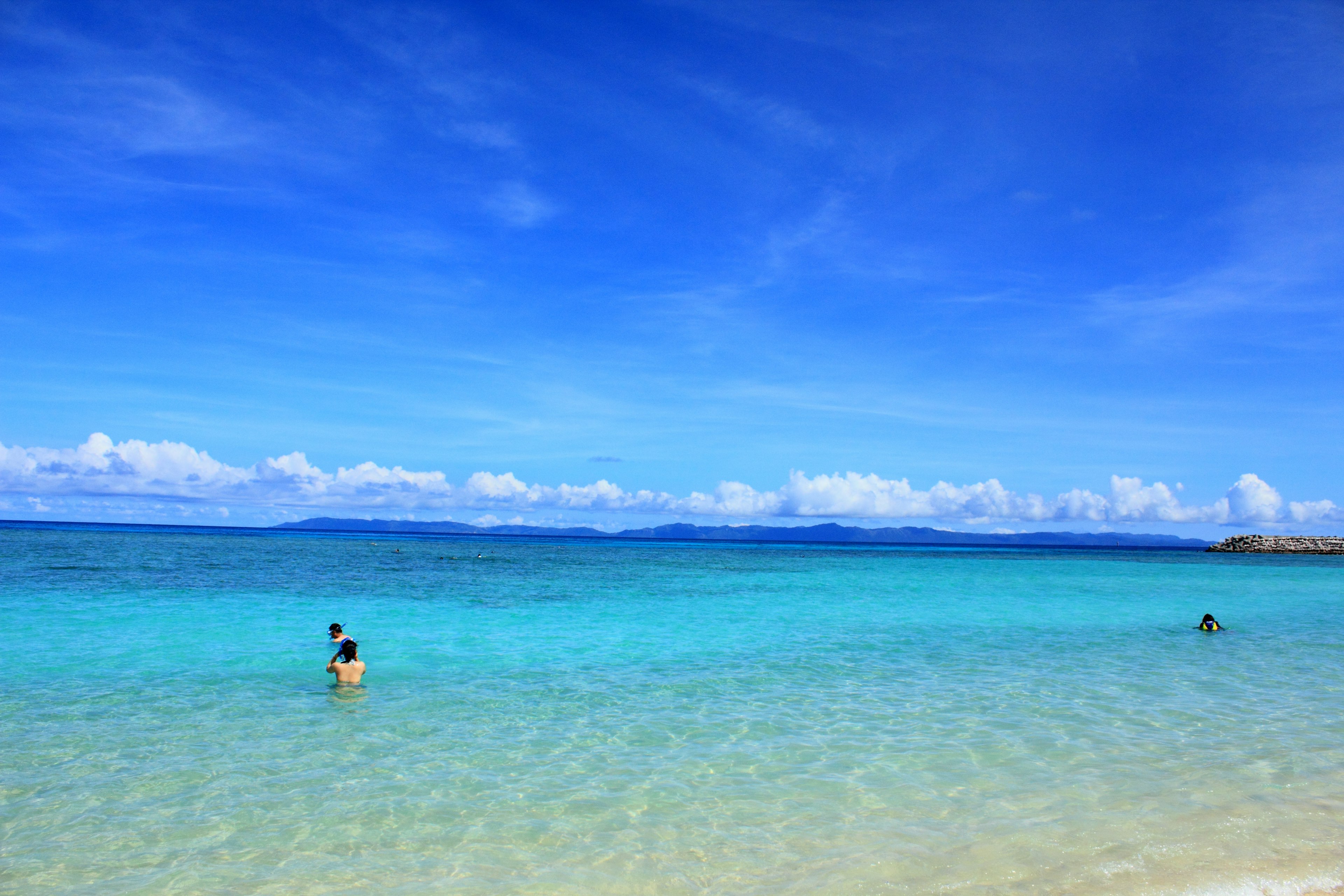 Orang-orang berdiri di pantai yang indah dengan laut dan langit biru