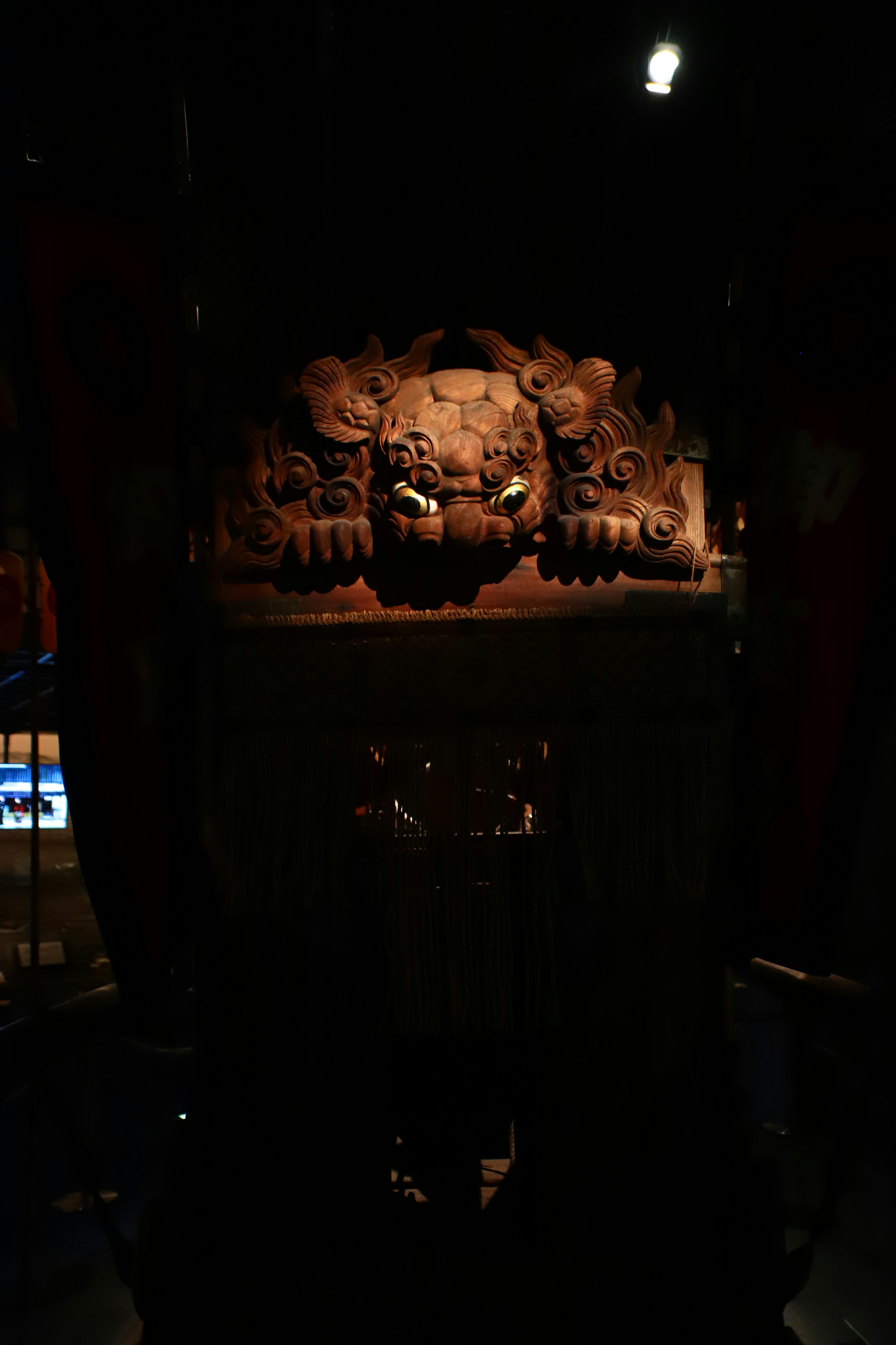 Carved lion head sculpture with an ornate pedestal in a dark setting