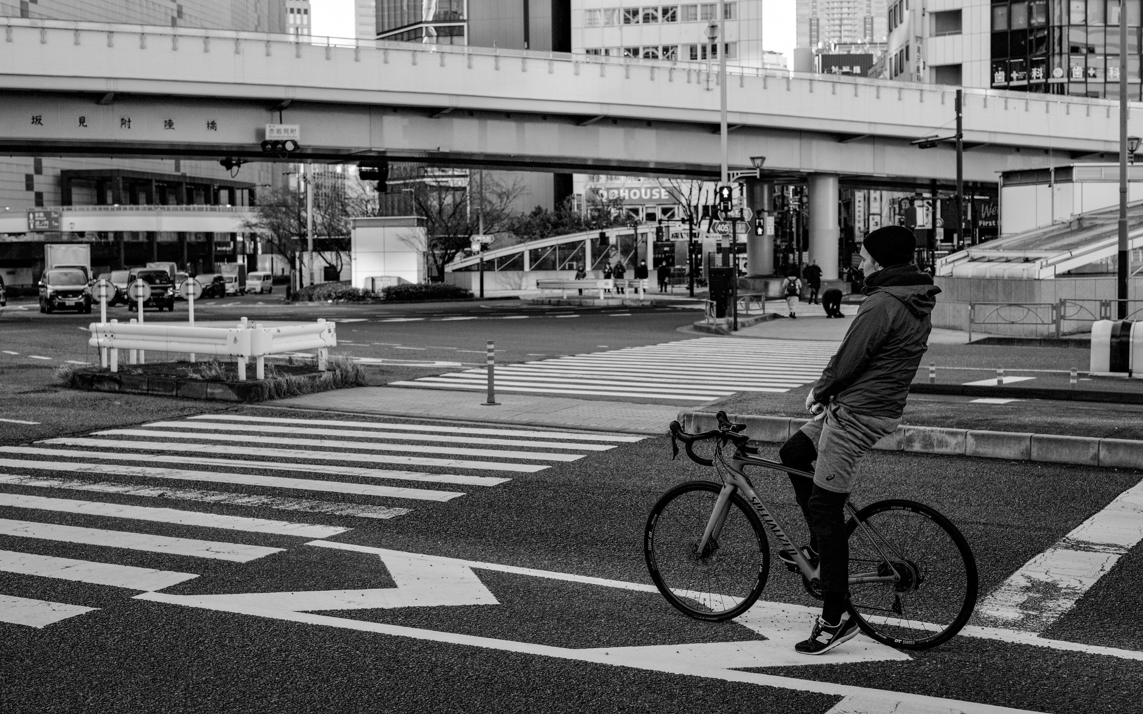 A person on a bicycle standing at a crosswalk in a monochrome urban setting