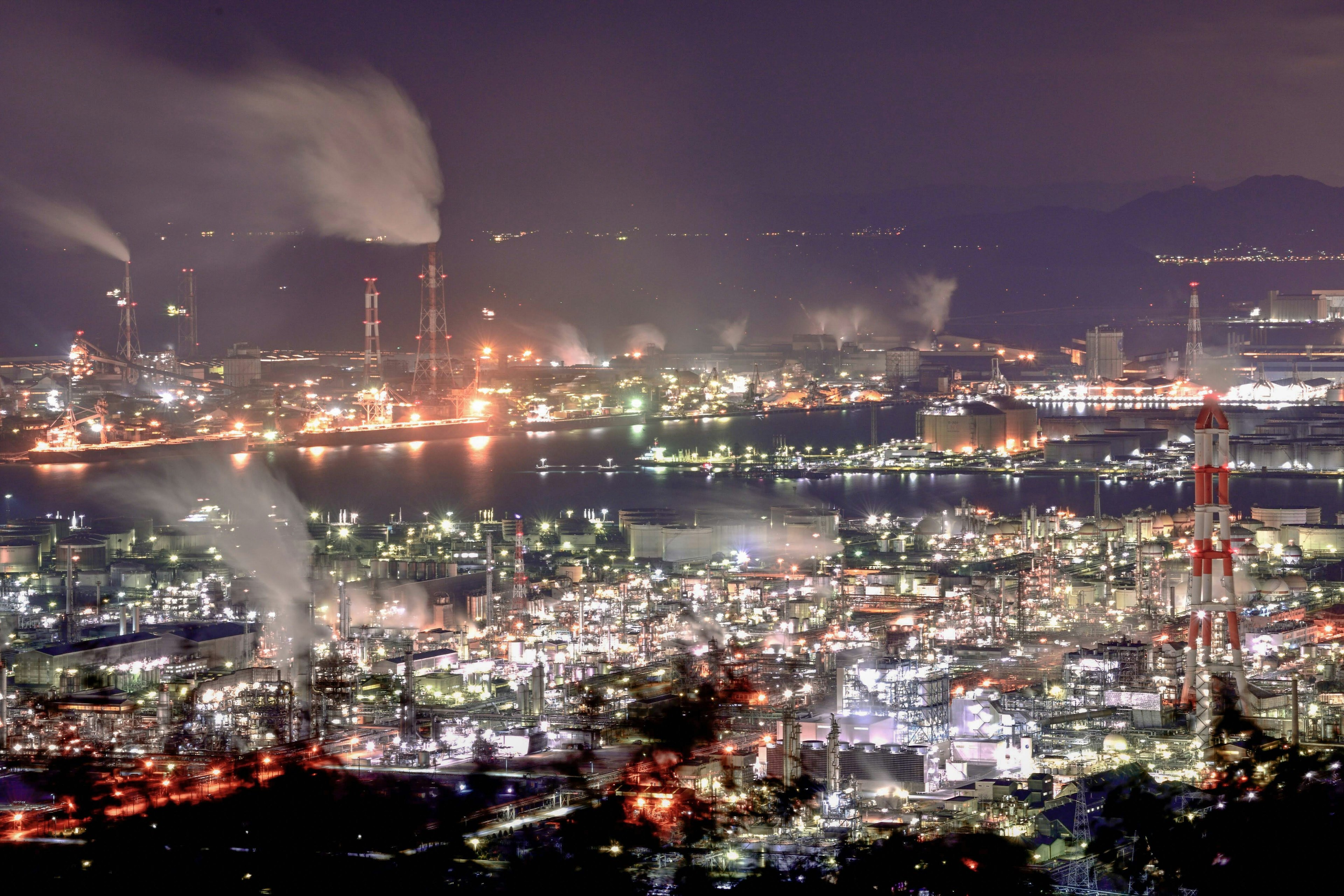 Nächtliche Aussicht auf ein Industriegebiet mit Rauch, der aus Schornsteinen aufsteigt, leuchtende Fabrikgebäude im Hintergrund