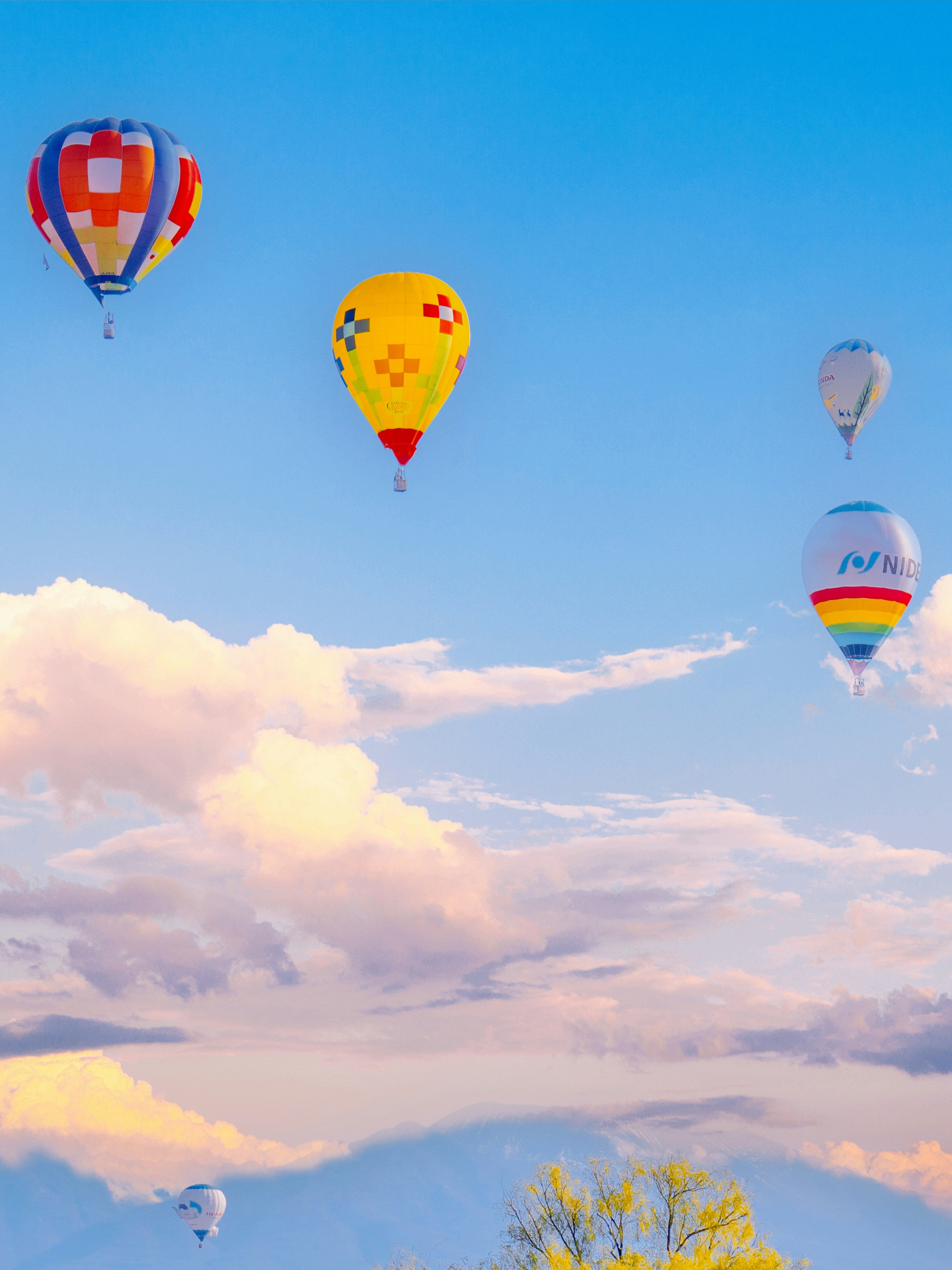 Balon udara panas berwarna-warni melayang di langit biru dengan awan yang tersebar