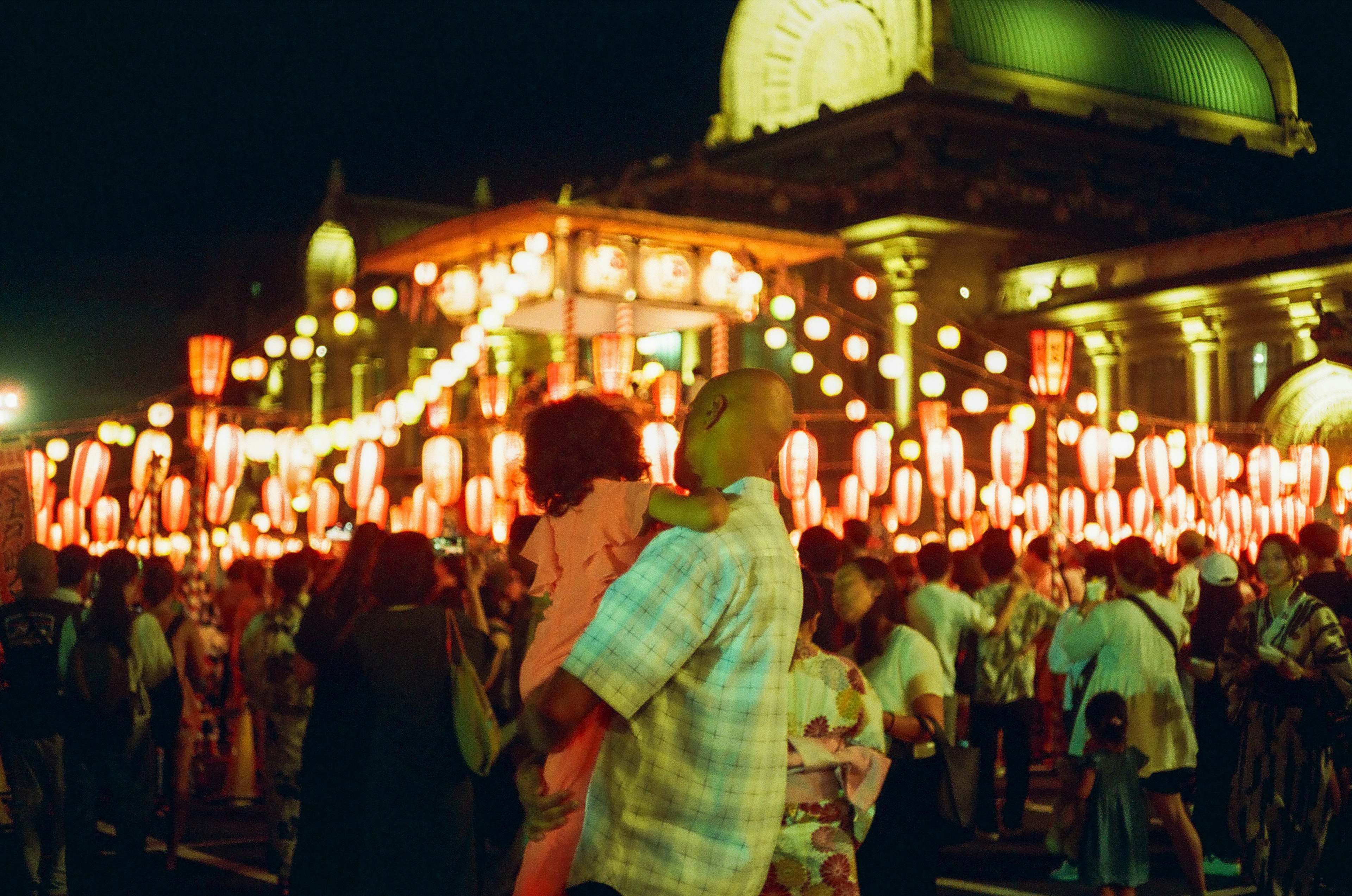 夜の祭りで赤い提灯の下に立つ人々と子供を抱える男性