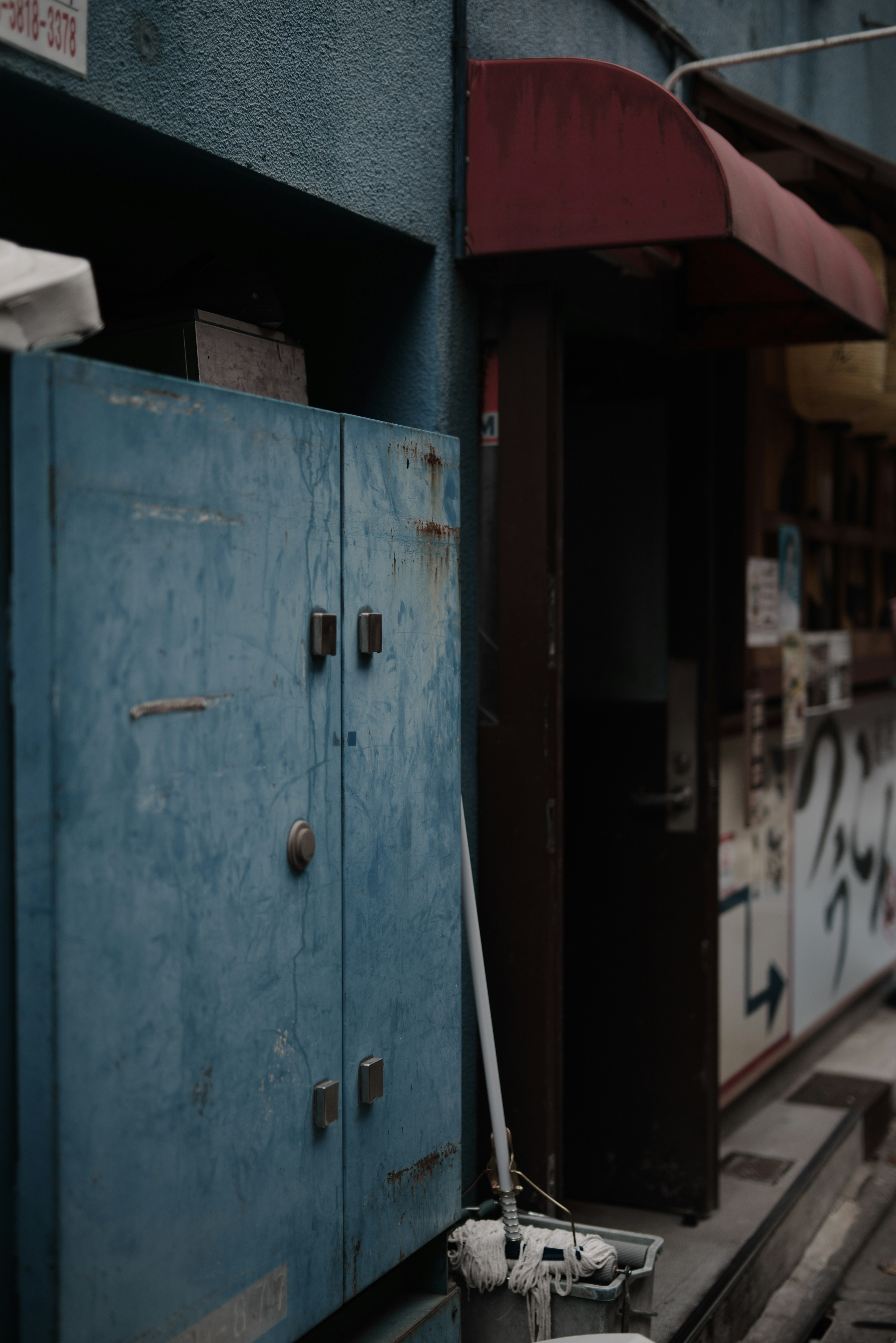 Boîte de rangement en métal bleue à côté d'une entrée de magasin avec un auvent rouge