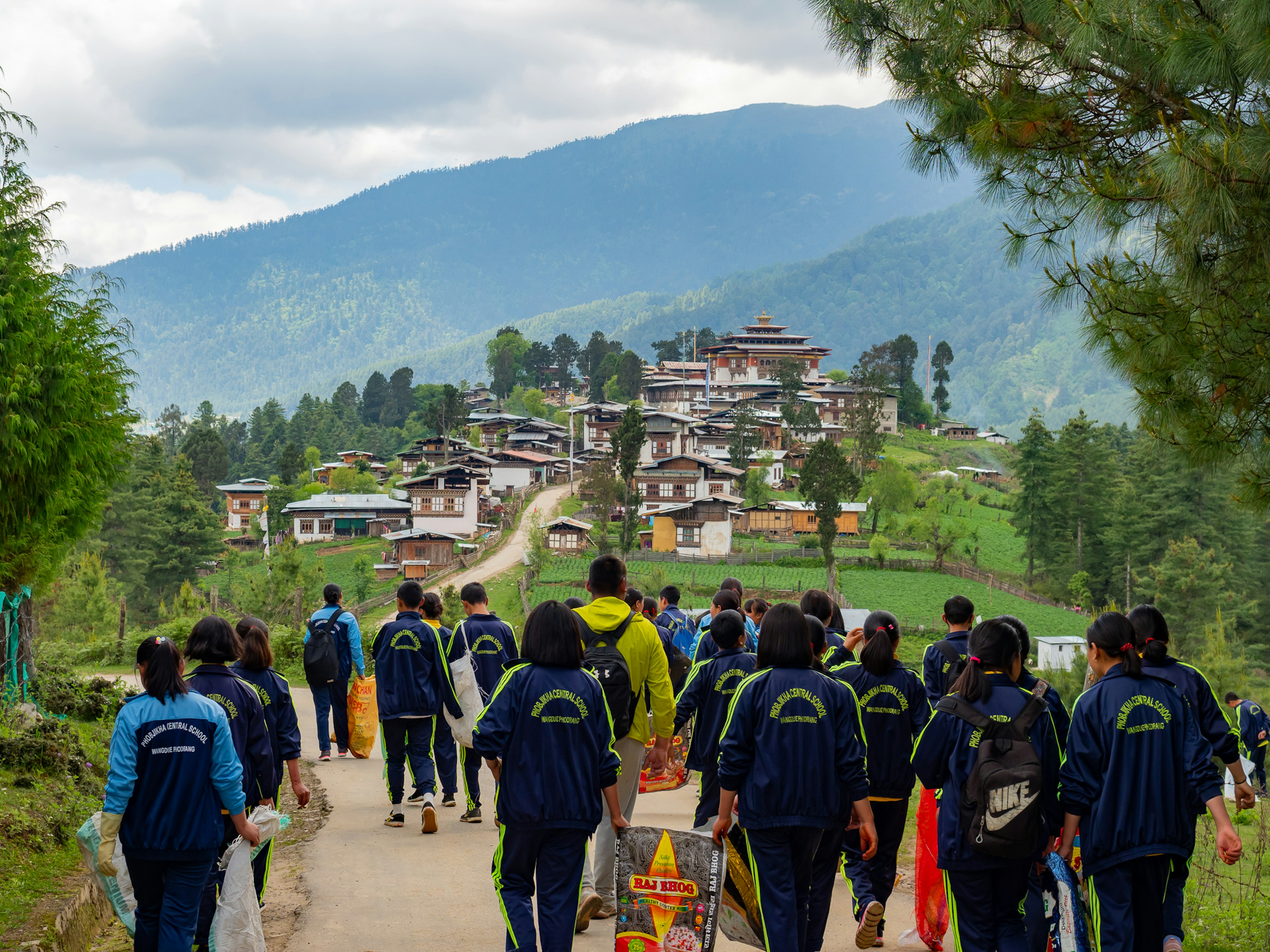 Studenti che camminano su un sentiero con un villaggio e montagne sullo sfondo