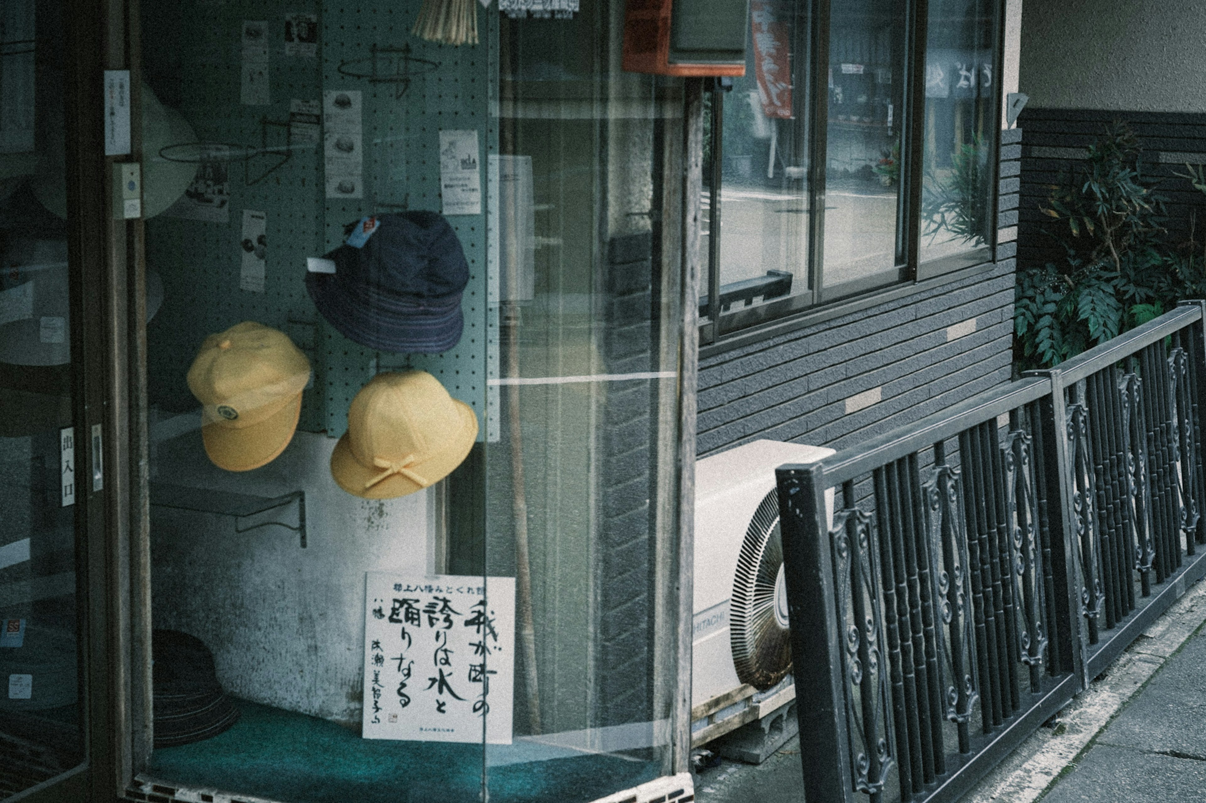 A shop corner with hats hanging behind a glass door and a handwritten sign