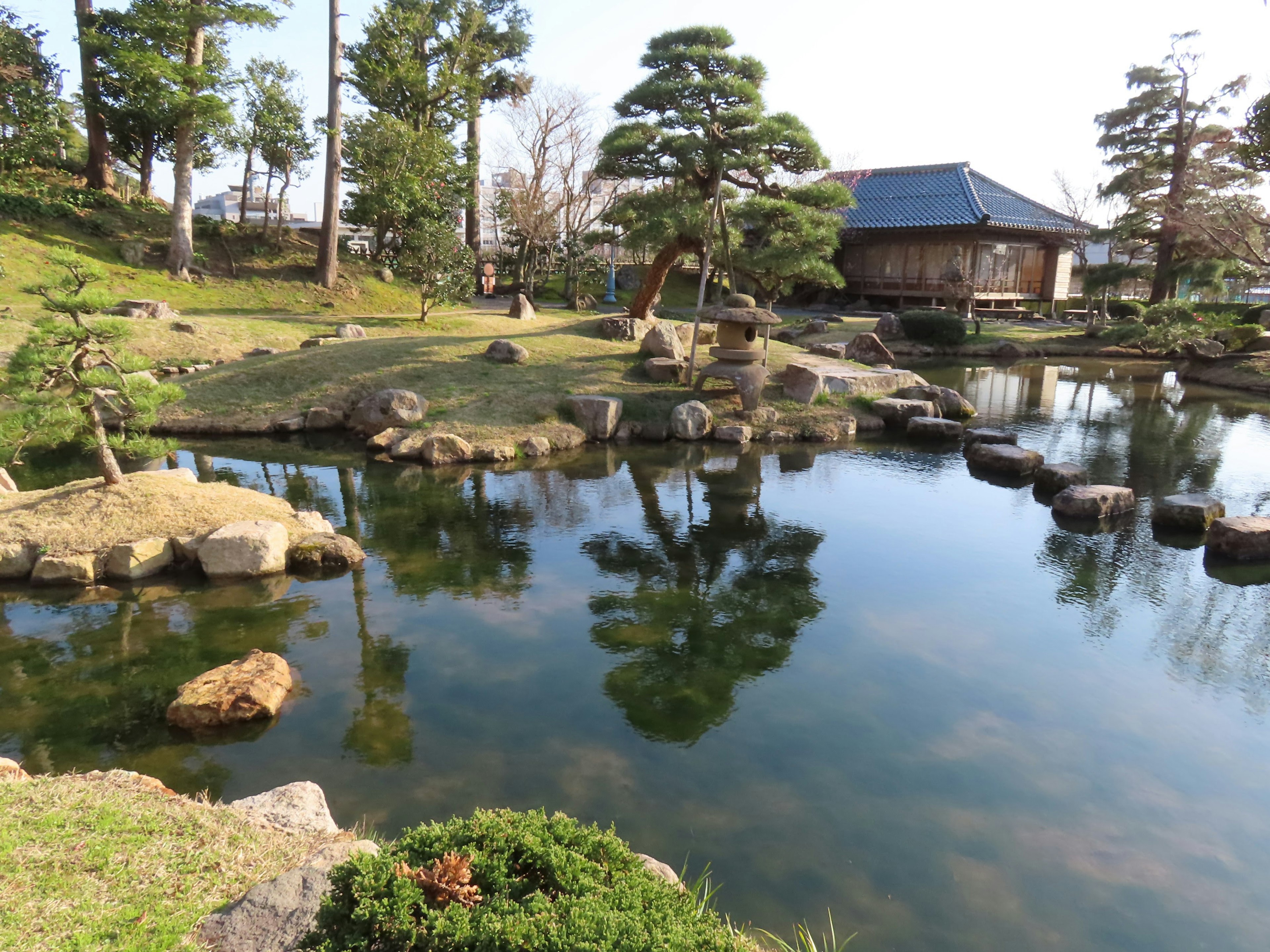 Ruhige japanische Gartenansicht mit Bäumen und Steinen, die im Teich reflektiert werden, Steinwegmerkmale