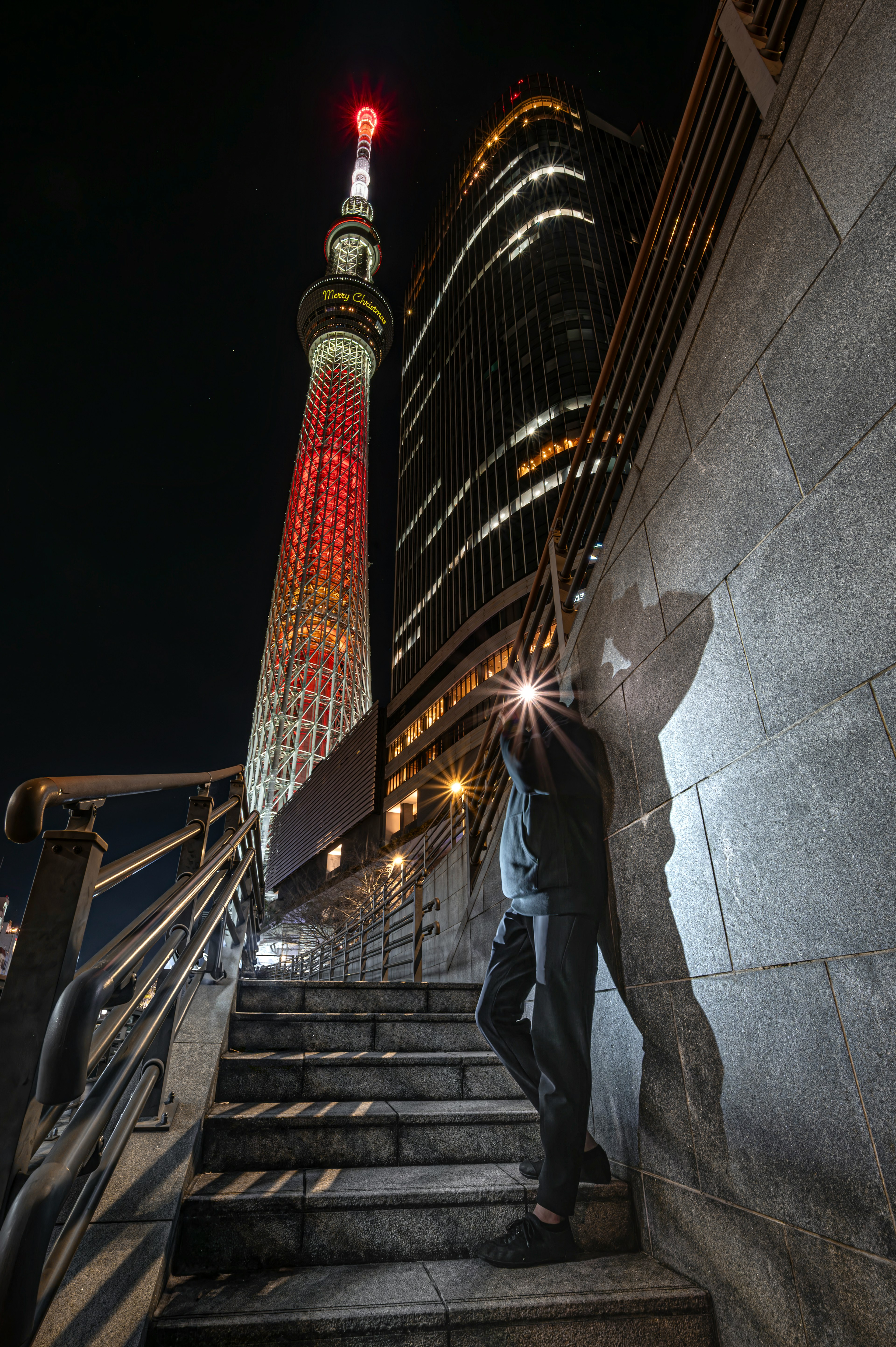 夜の東京スカイツリーのライトアップと階段を登る人物