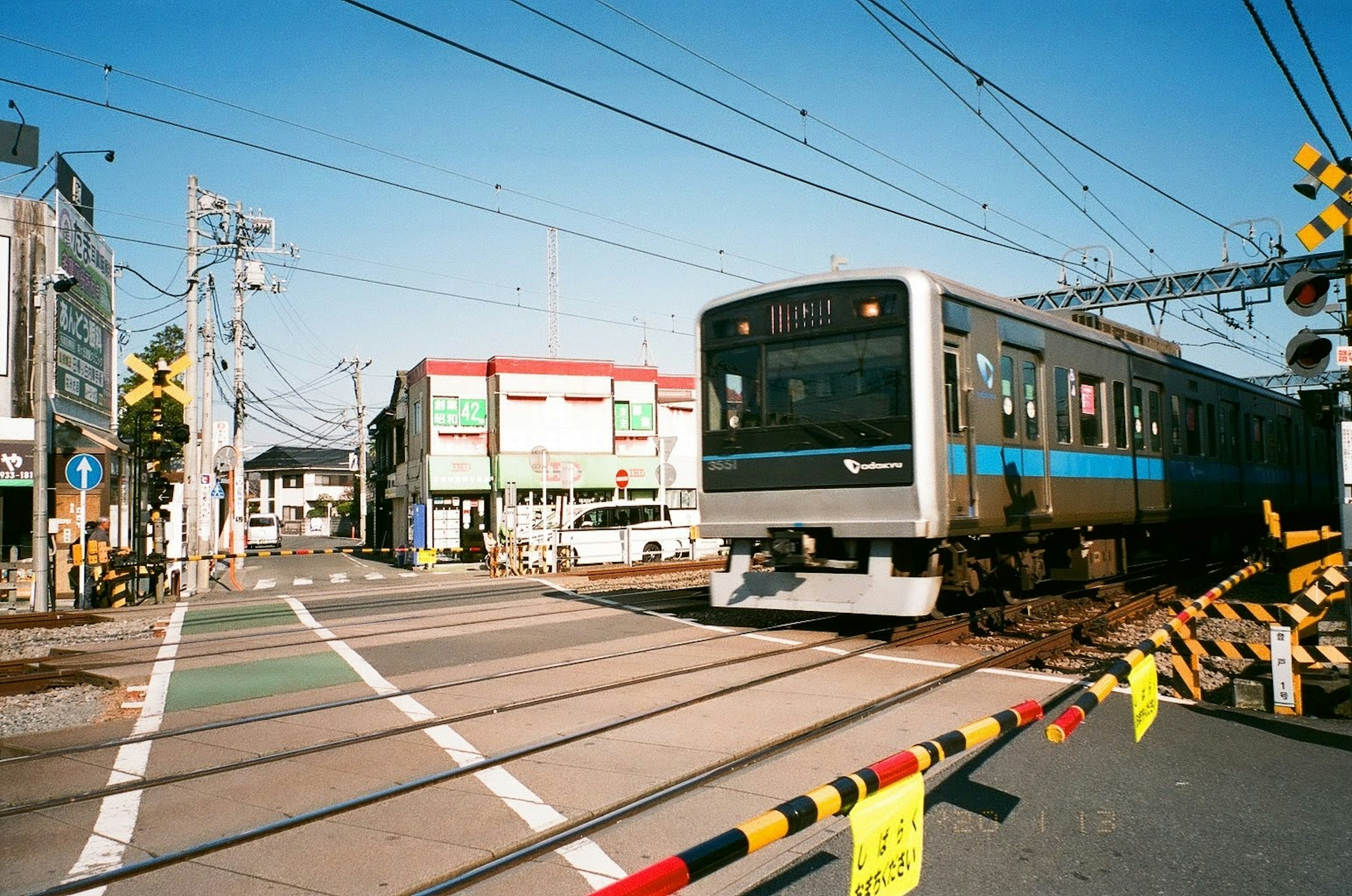 青空の下で走行中の列車と踏切の風景