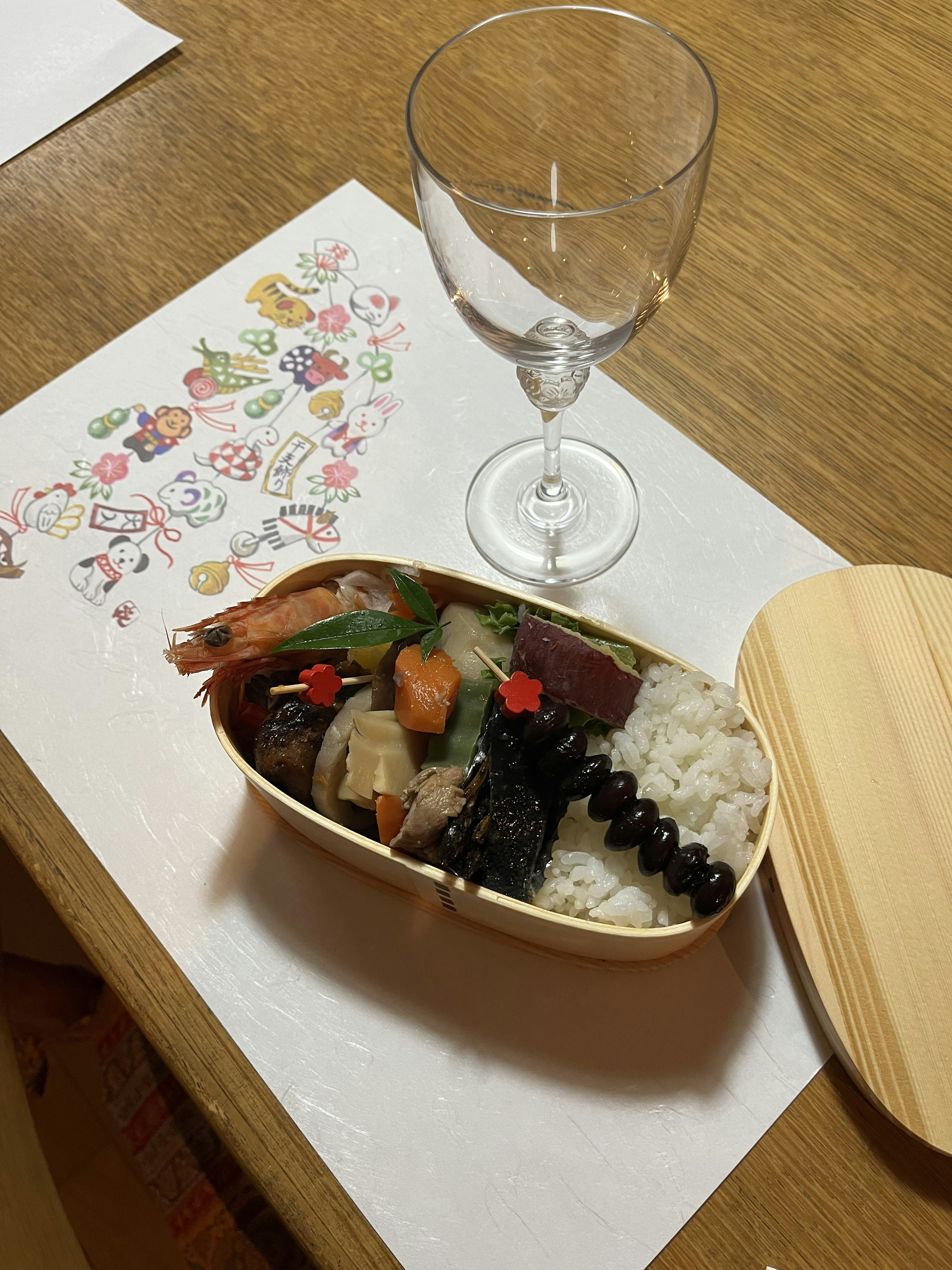 A beautifully arranged bento box with colorful dishes and a glass on a table