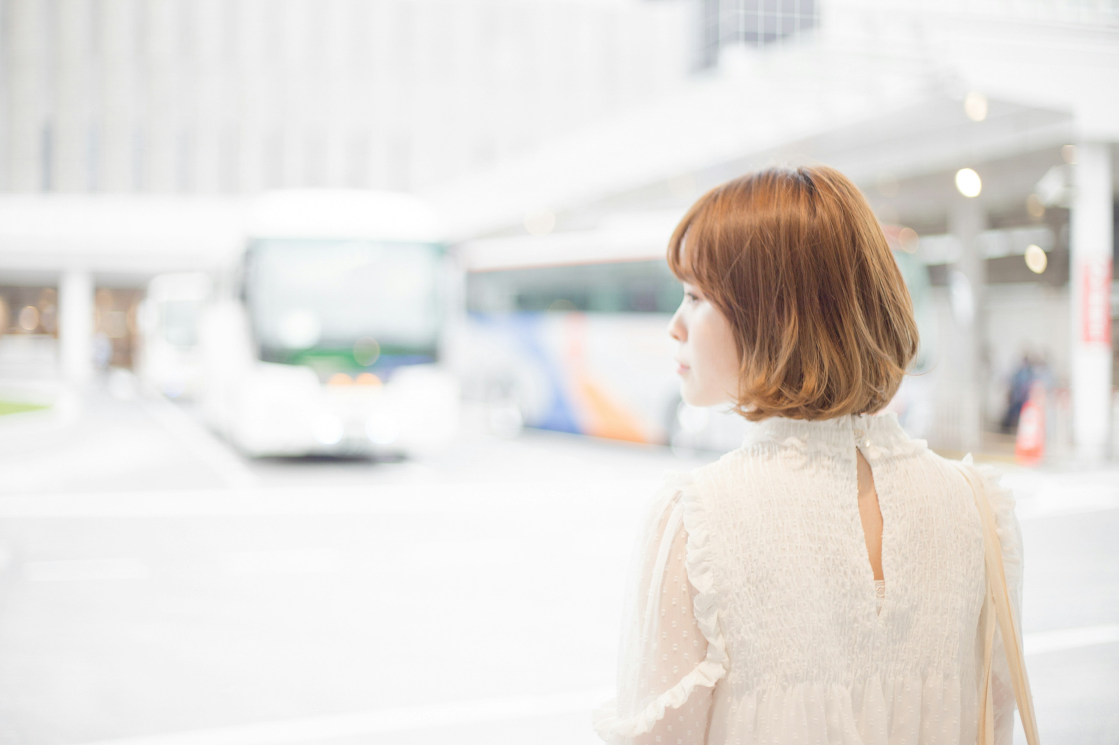 A woman with short hair looking at a bus in a bright urban setting