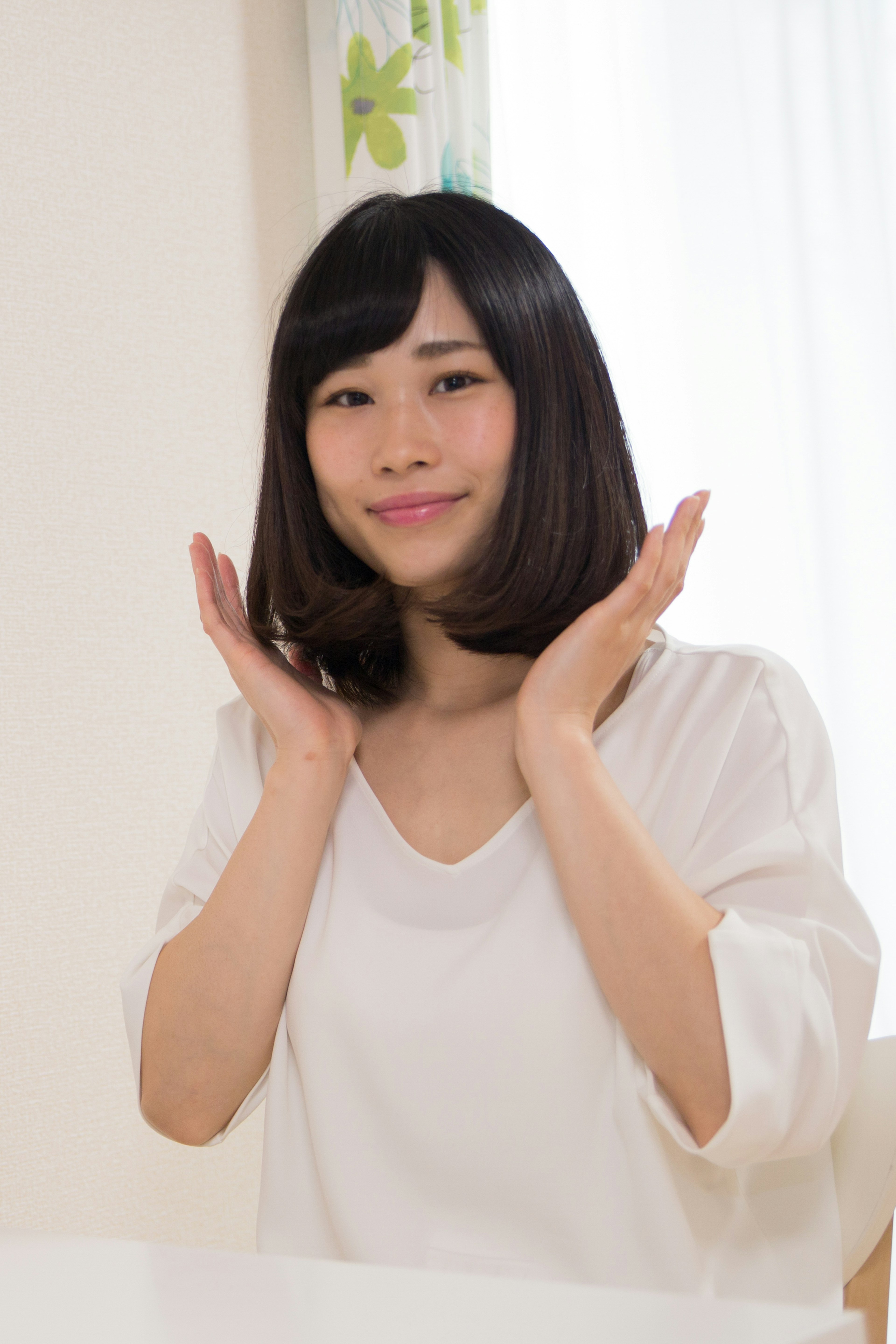 Une femme en chemise blanche souriant avec les mains sur les joues